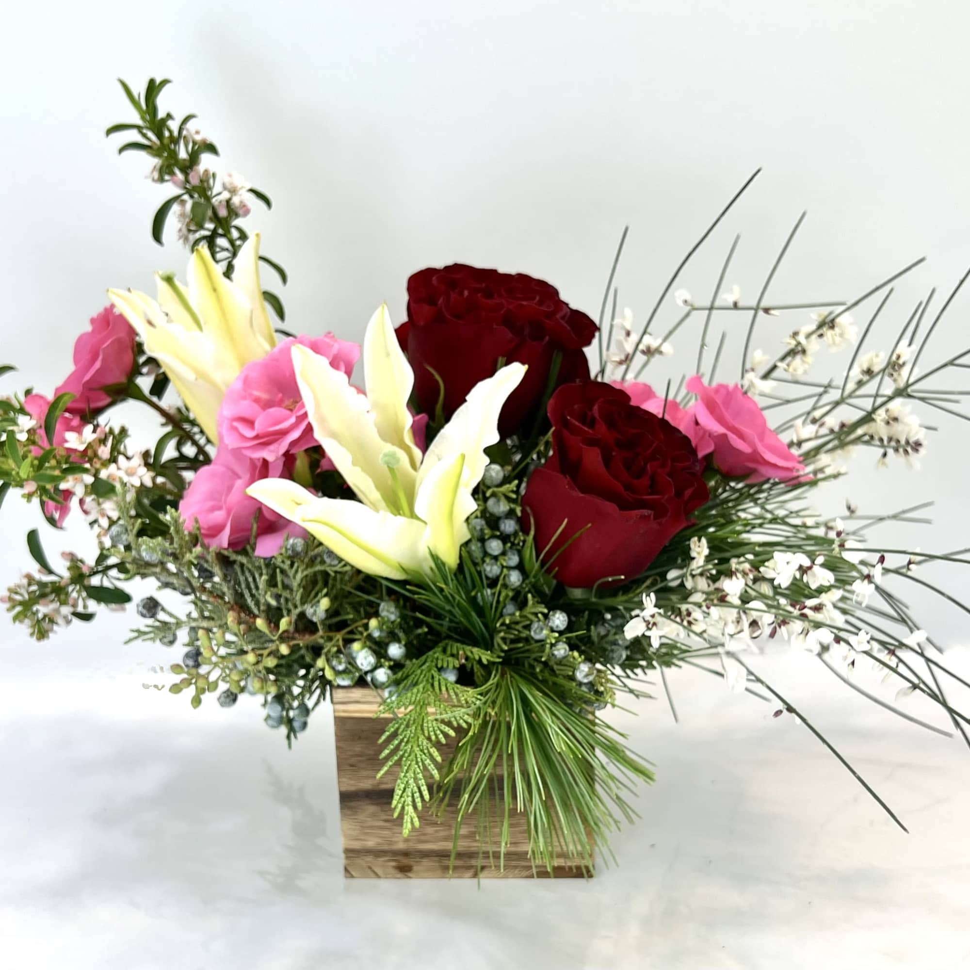 Arrangement of red and pink roses with white lilies in a wooden box