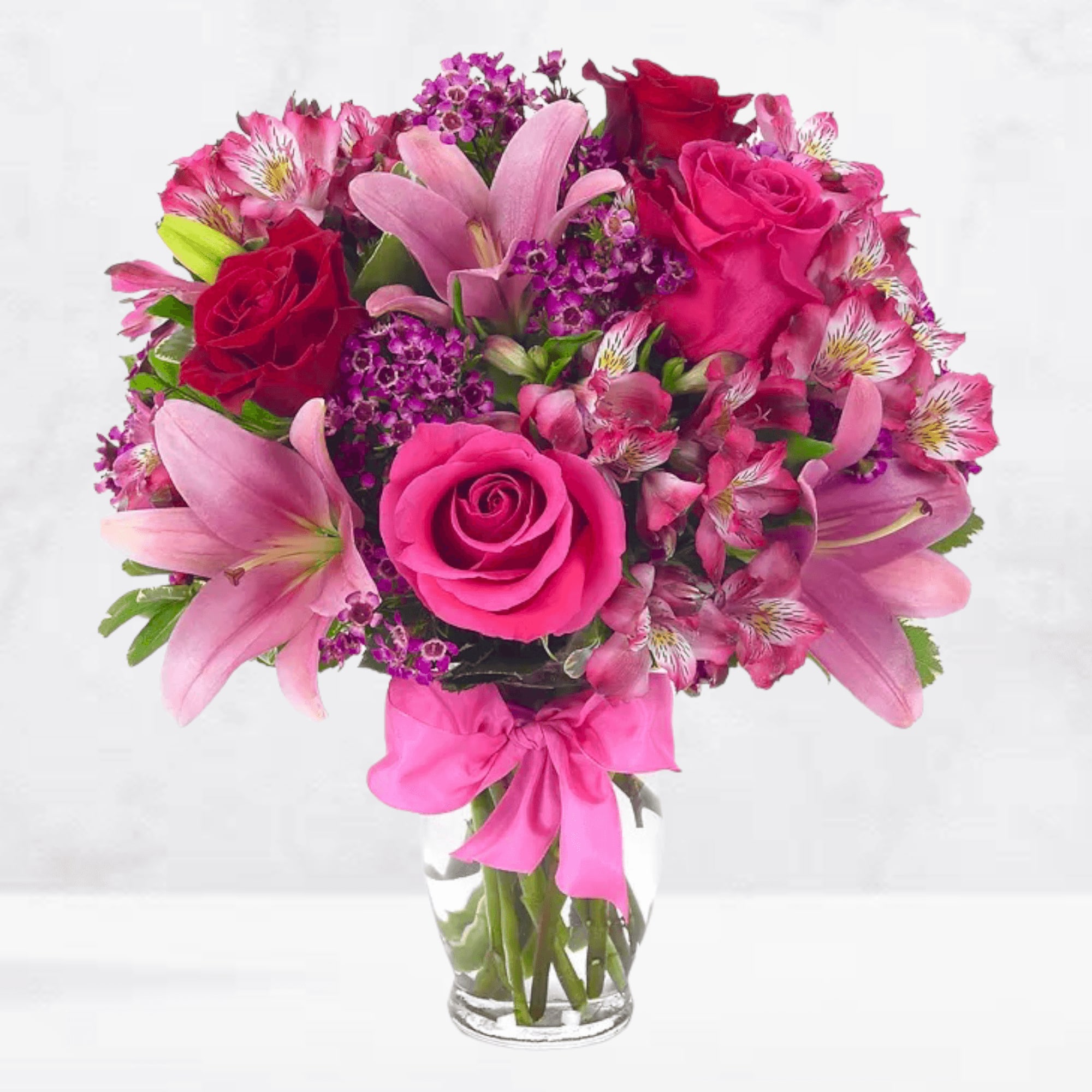 Pink and red mixed flower bouquet in a clear glass vase with a pink ribbon
