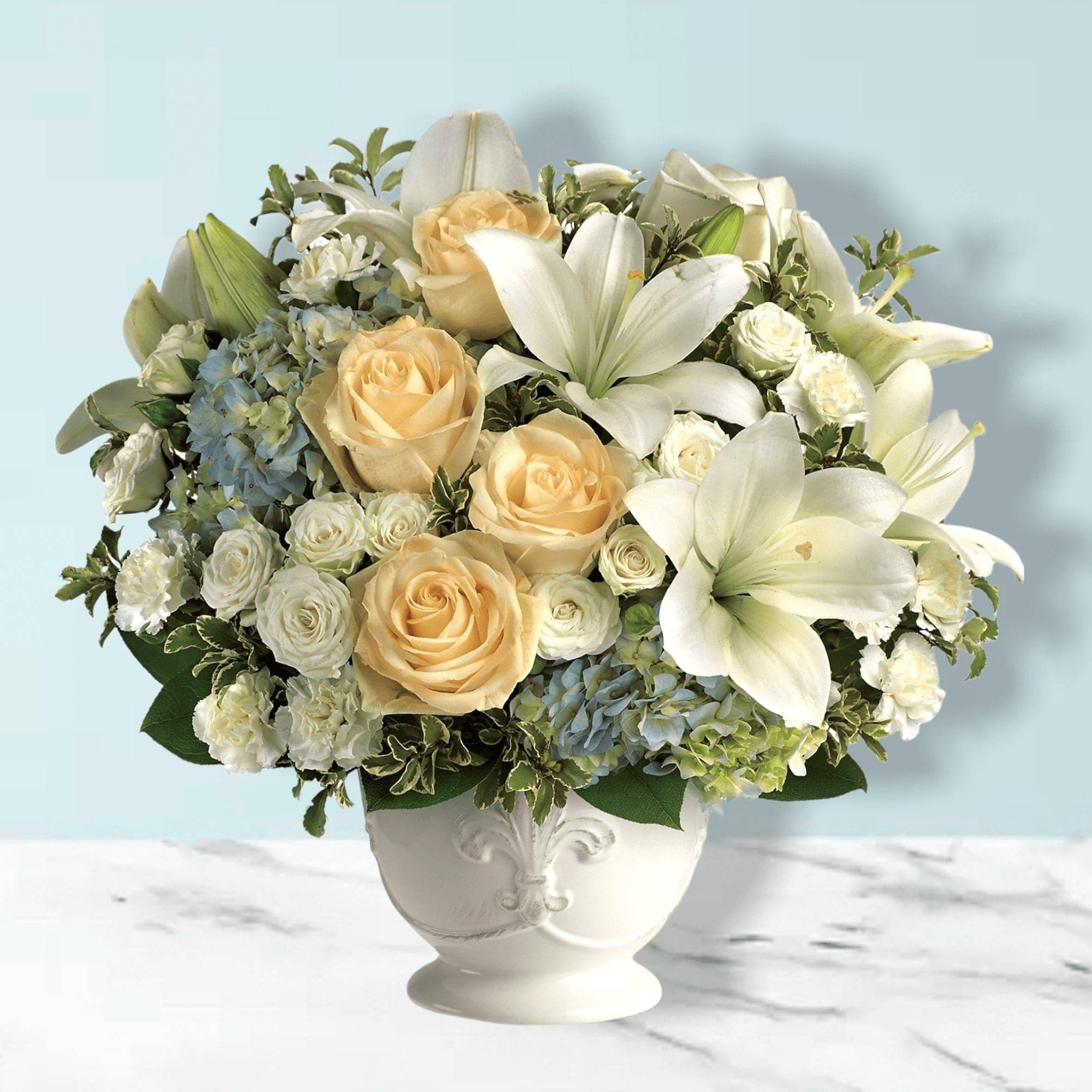 Cream roses and white lilies arranged in a white vase