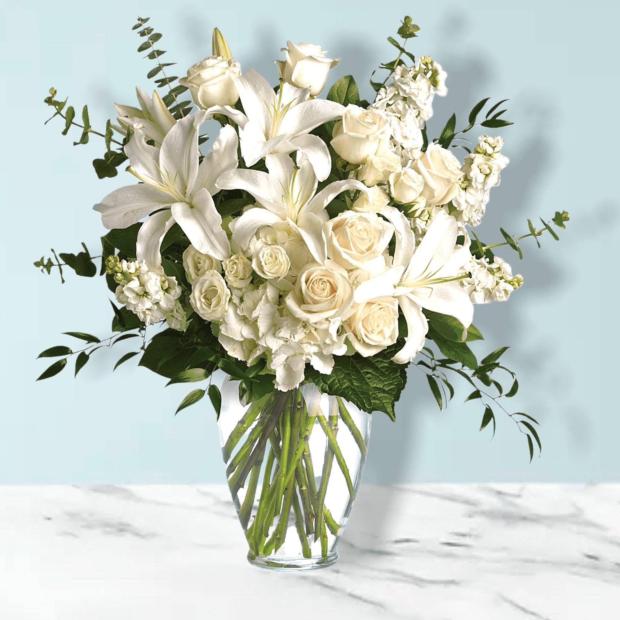 White lilies and roses arranged in a clear glass vase