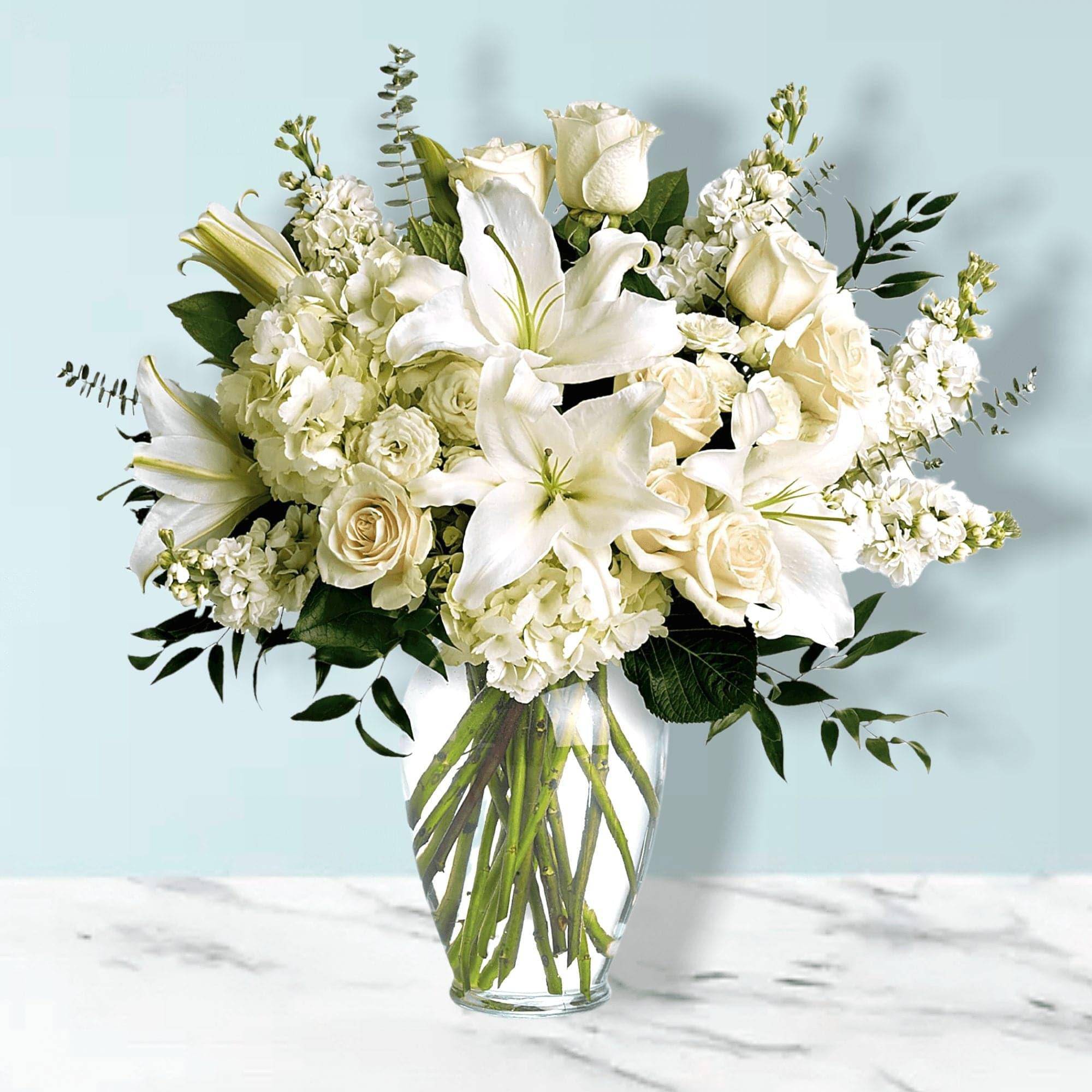 White lilies and roses arranged in a clear glass vase