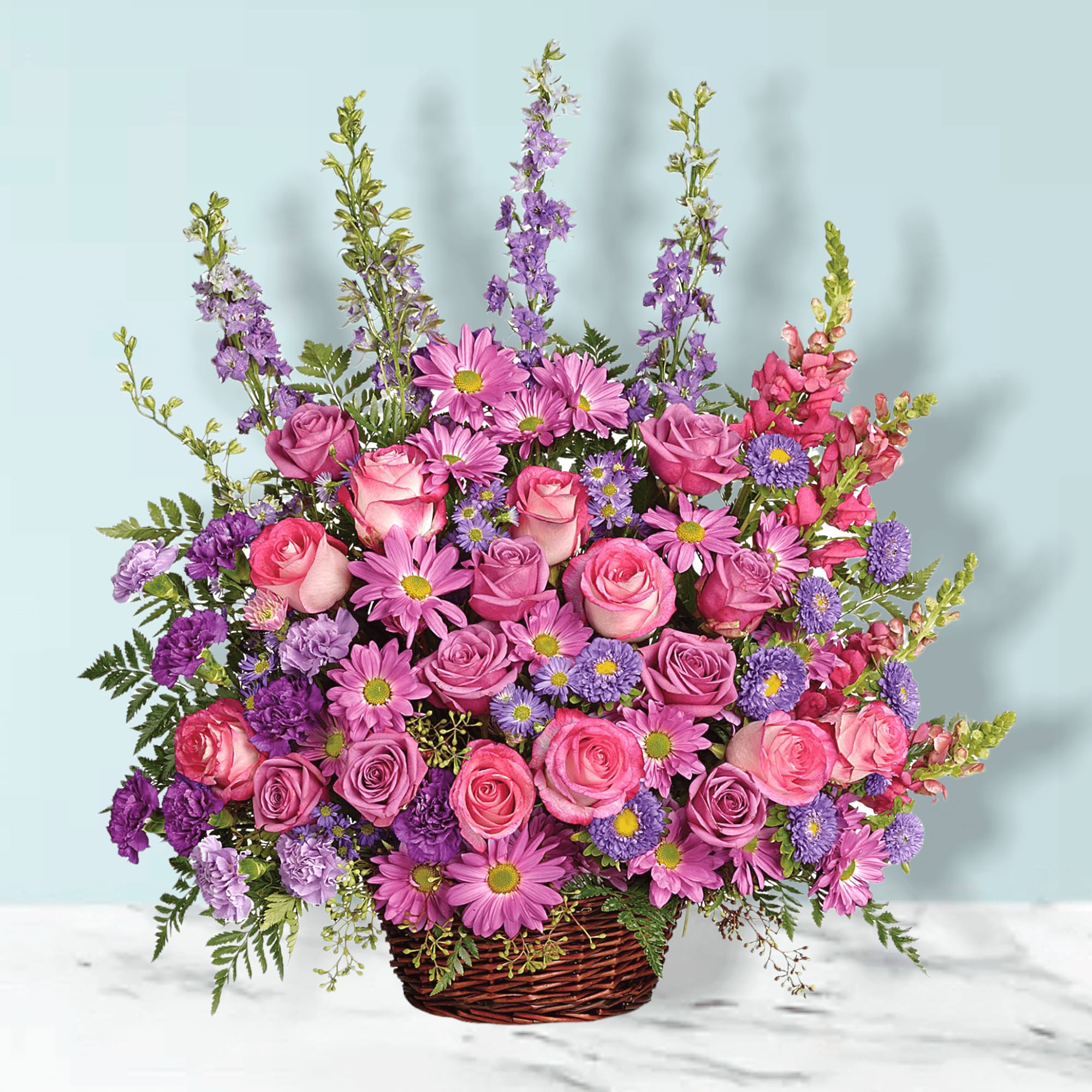 Basket arrangement of pink roses, purple daisies, and snapdragons