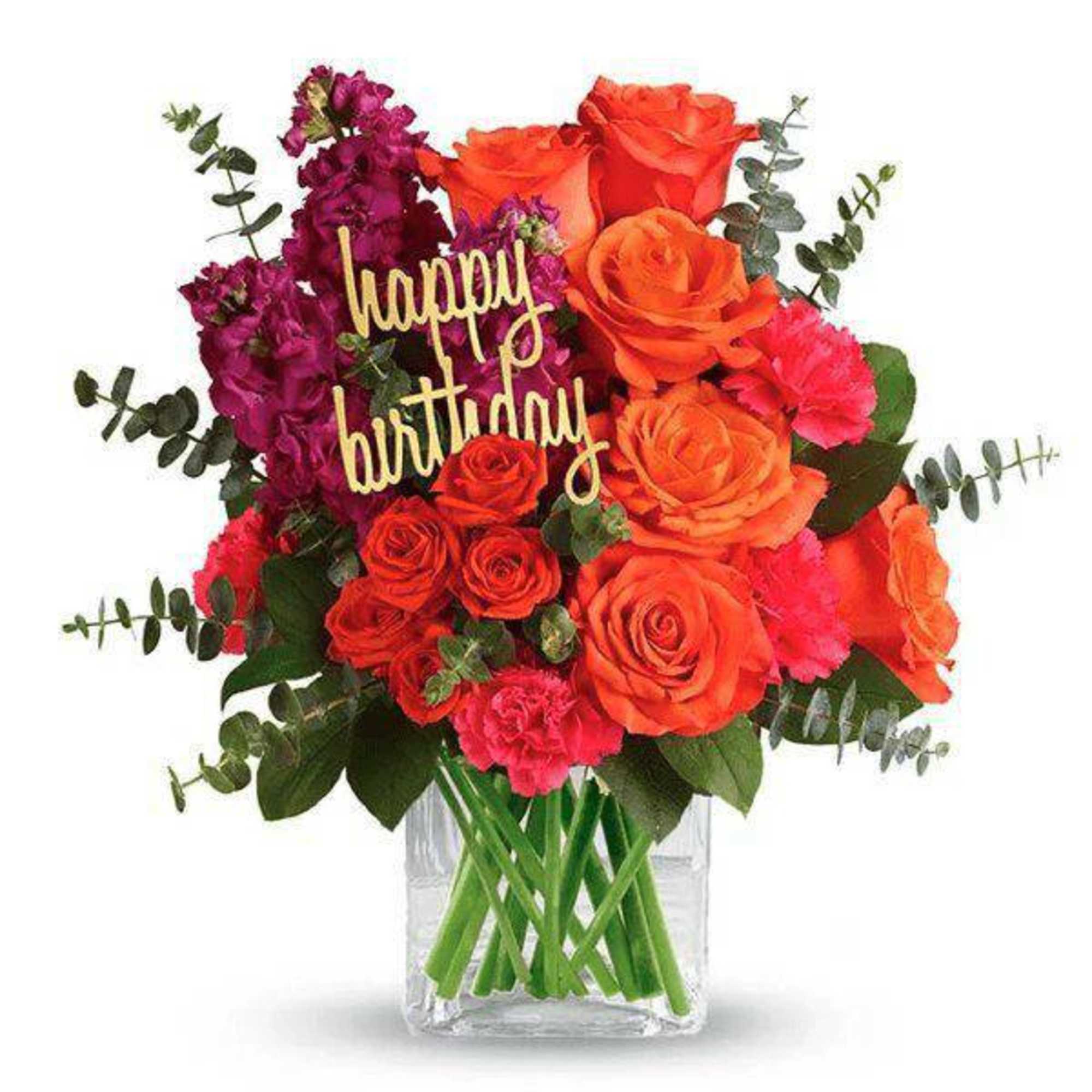 Bouquet of orange and magenta flowers in a clear glass vase with a happy birthday sign