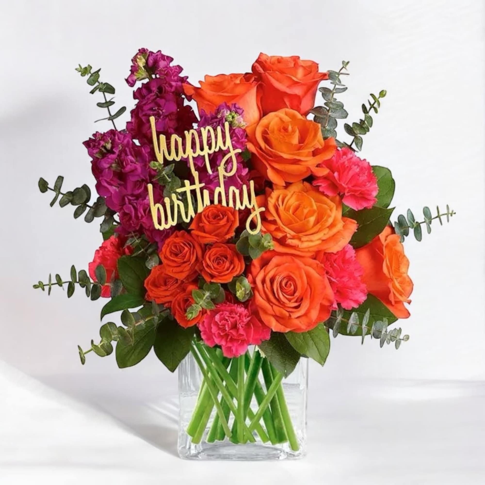Bouquet of orange and pink flowers in a clear vase with a happy birthday sign