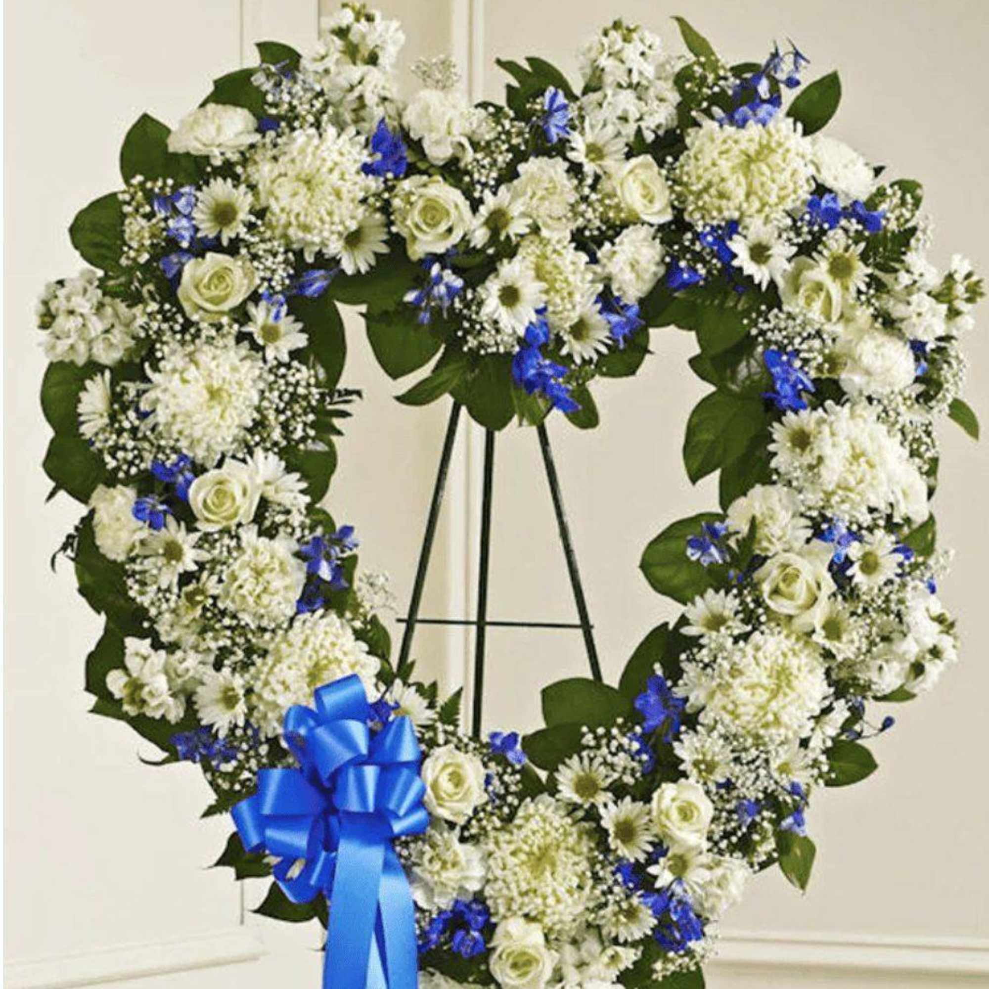 Heart-shaped white and blue floral wreath on a stand with a blue ribbon