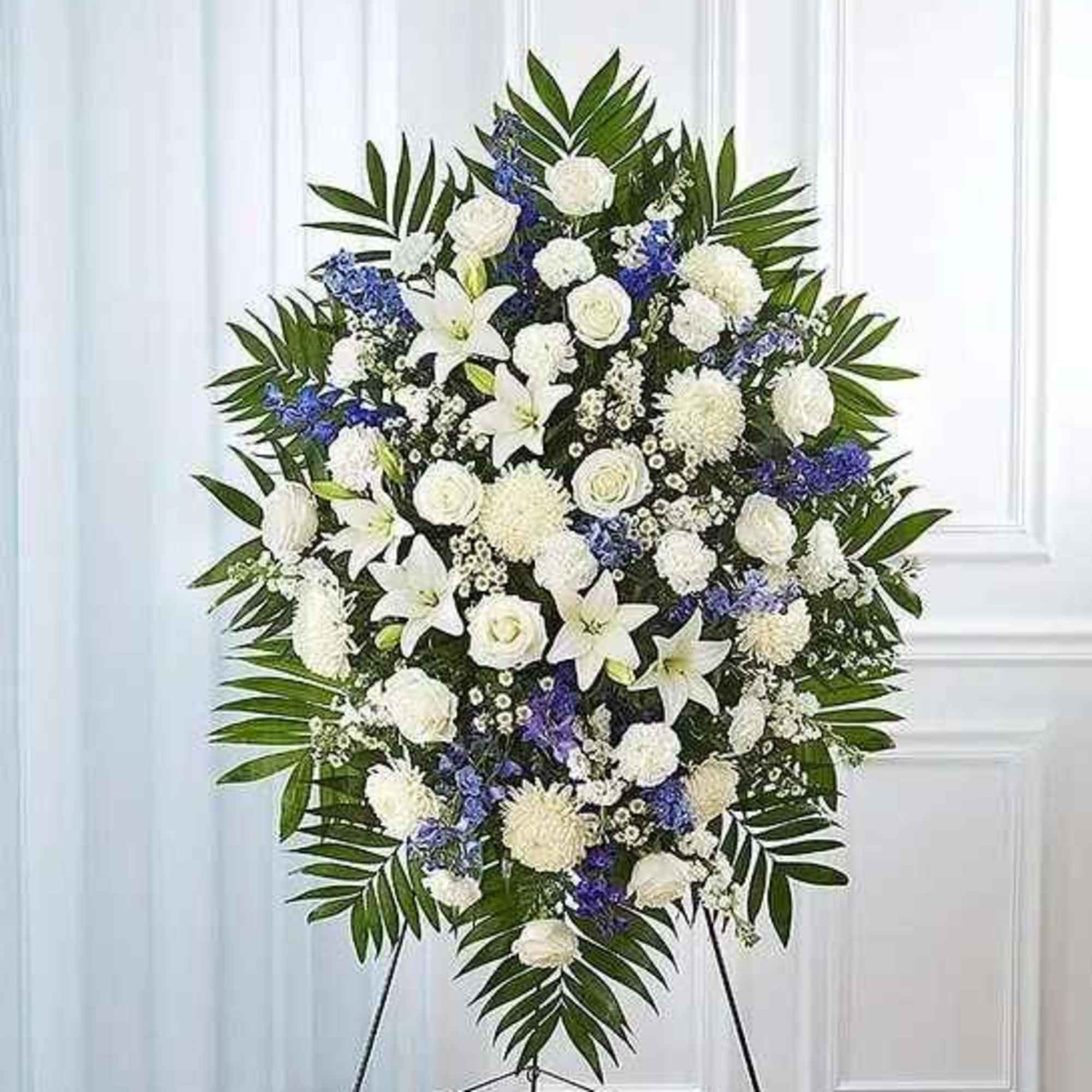 White and blue funeral spray on a stand with palm fronds