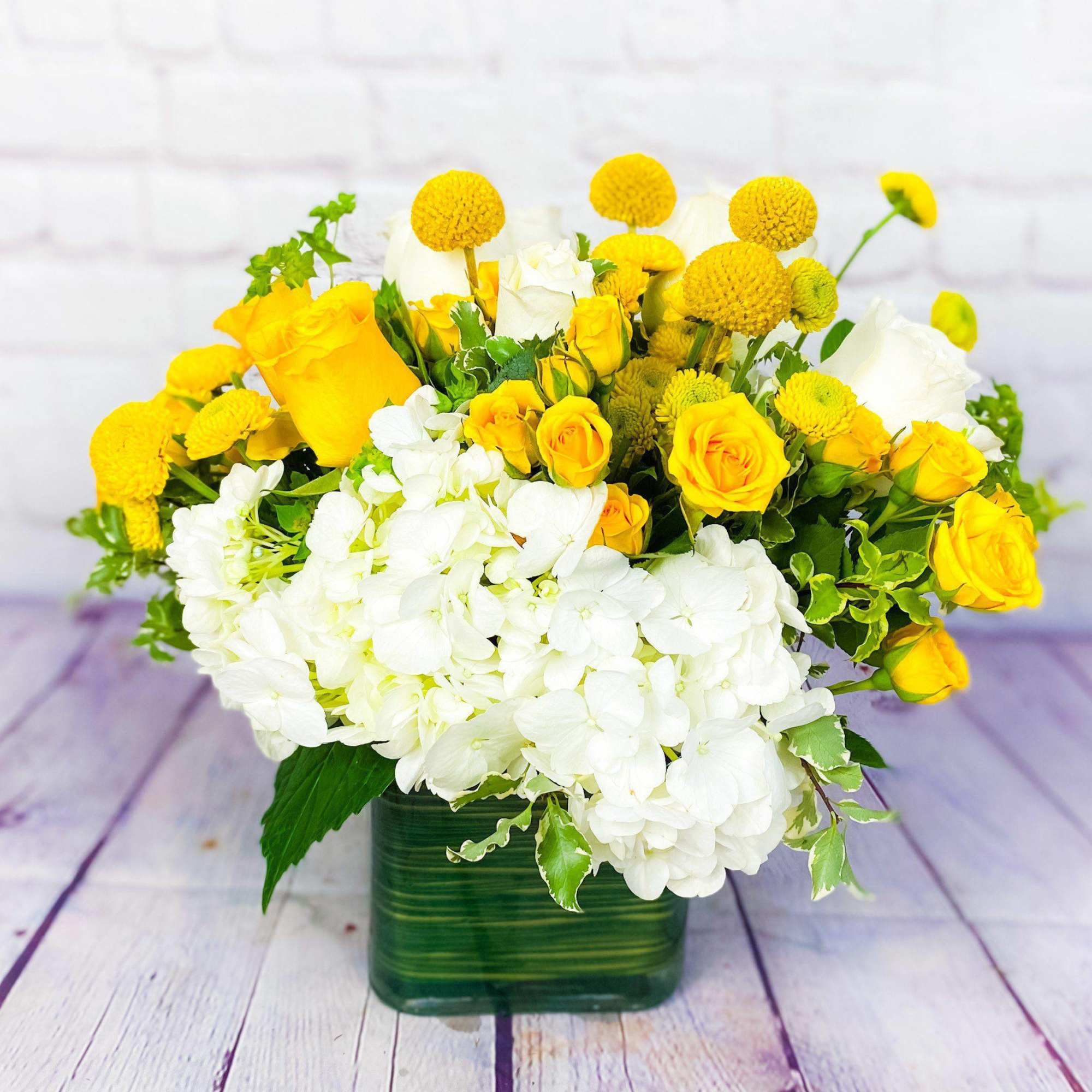Yellow roses and white hydrangeas in a green glass vase
