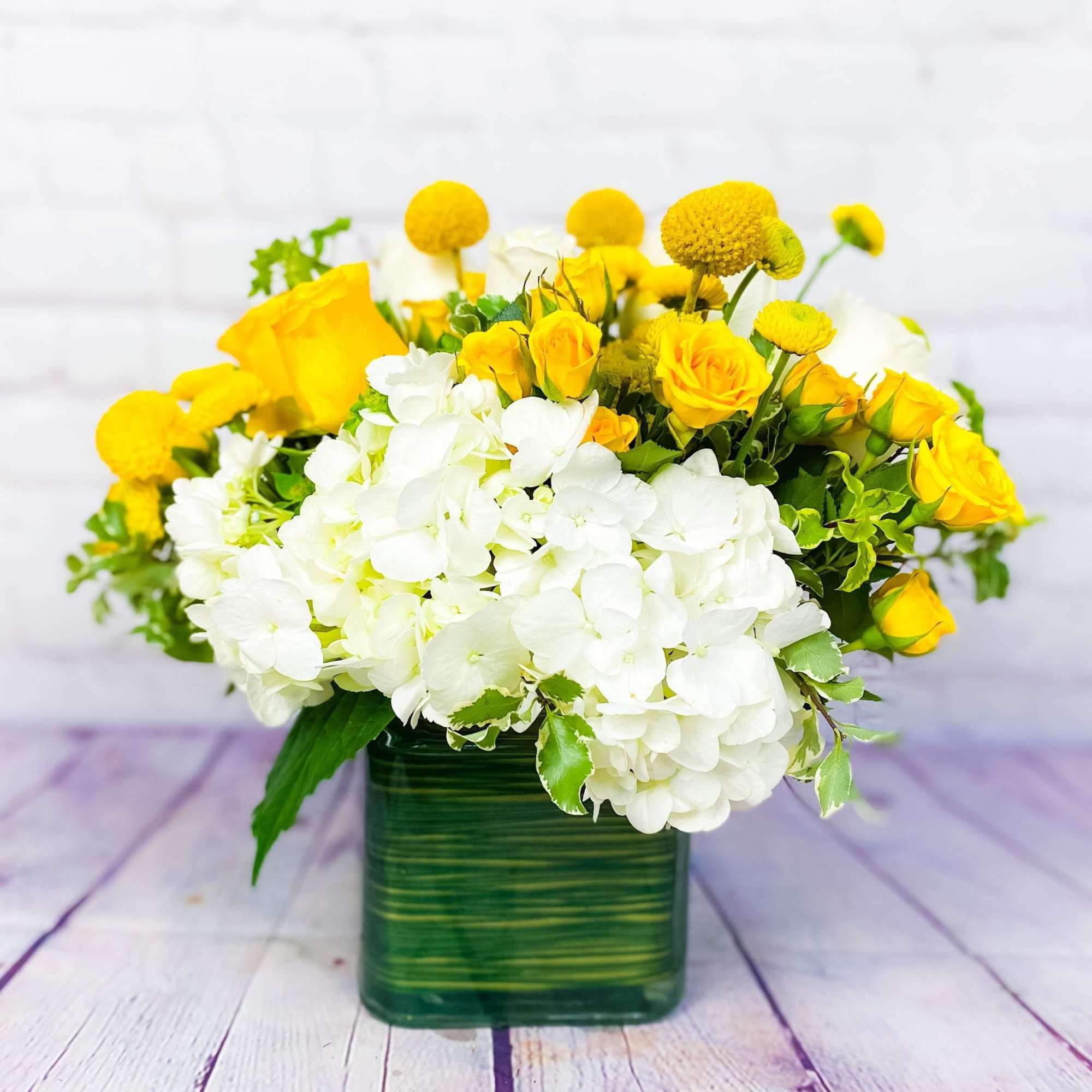 Yellow roses and white hydrangeas in a green square vase