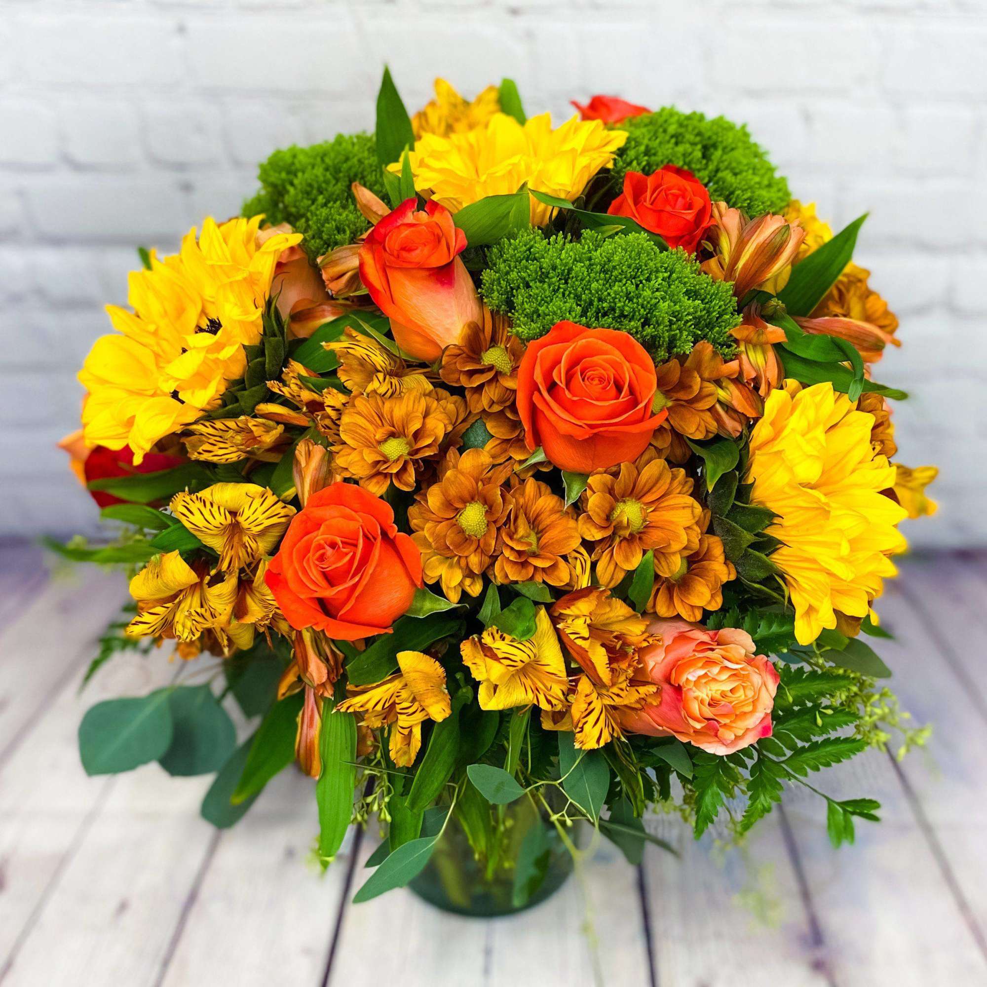 Bouquet of orange roses, yellow blooms, and green pompons in a glass vase