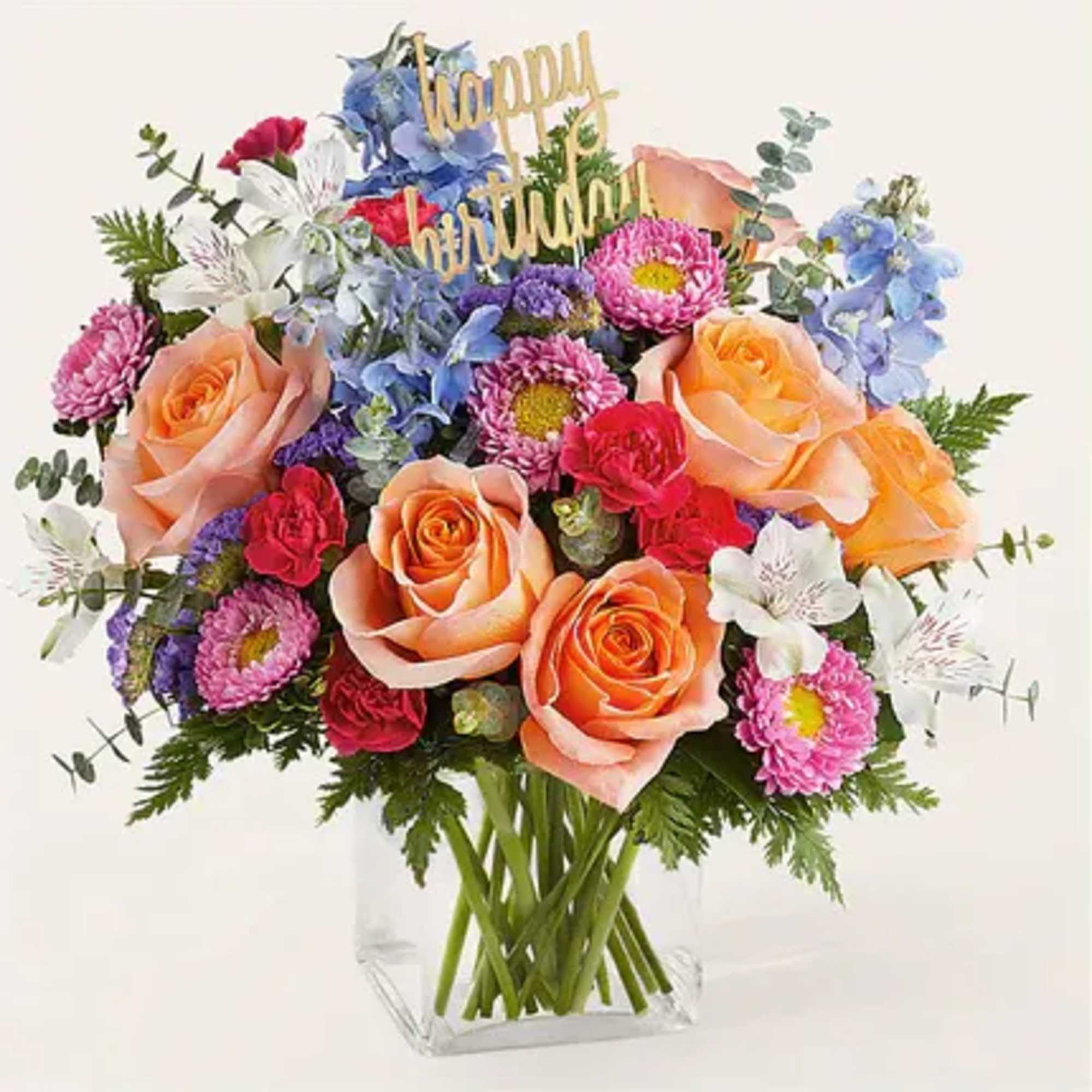 Colorful bouquet of roses, daisies, and mixed blooms in a clear vase with a "happy birthday" topper