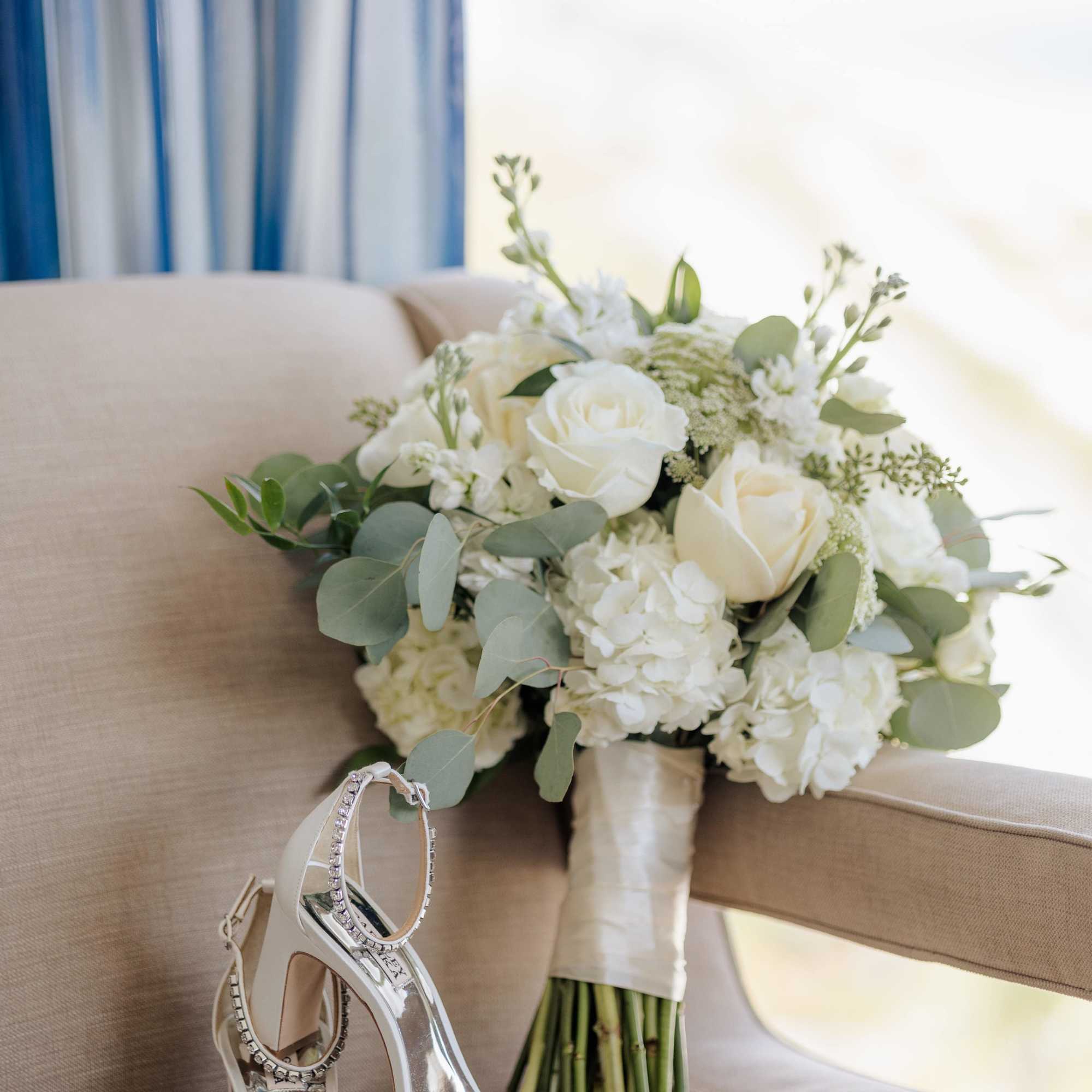 White rose bouquet with greenery beside jeweled high-heeled sandals