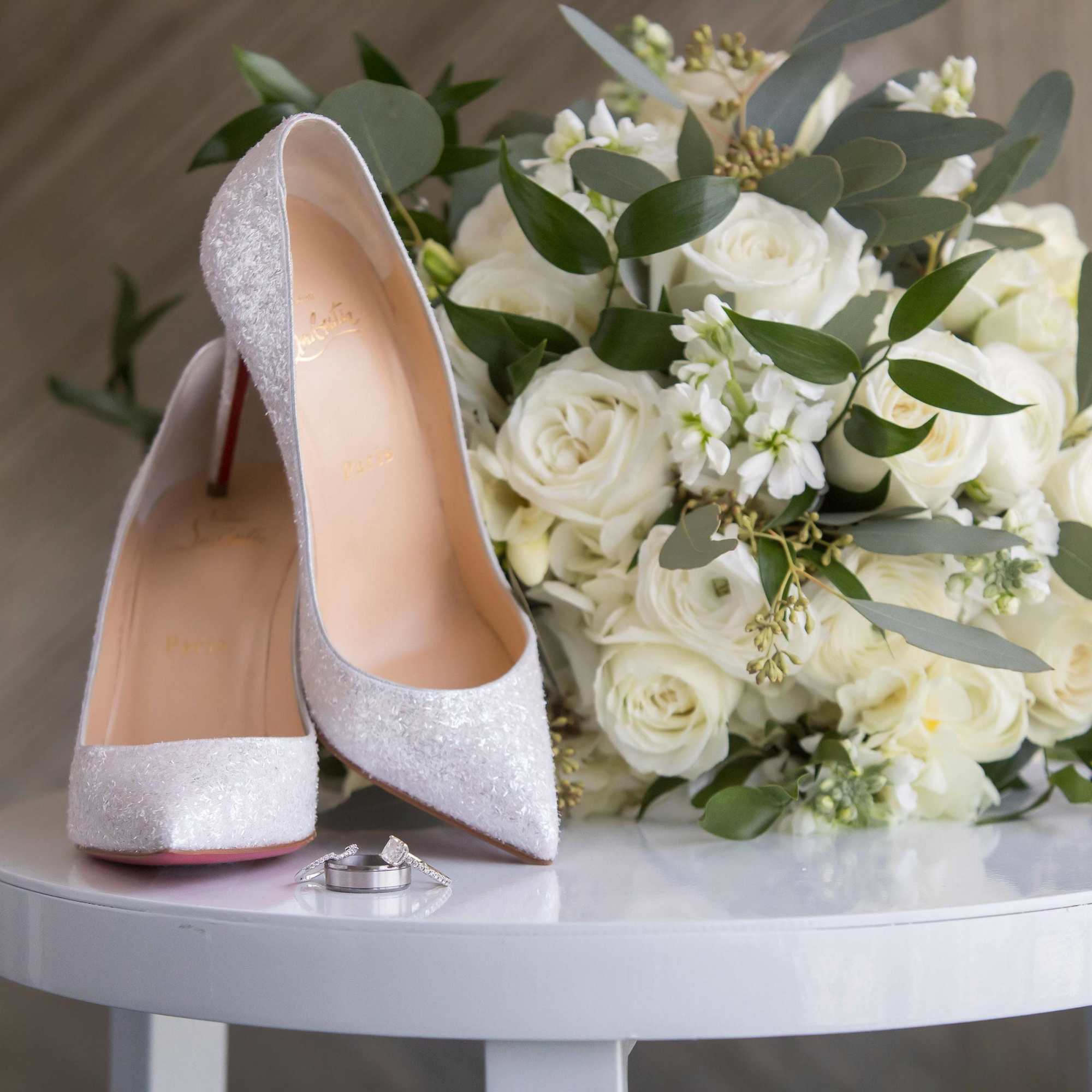 White rose bouquet with silver high heels and wedding rings on a table