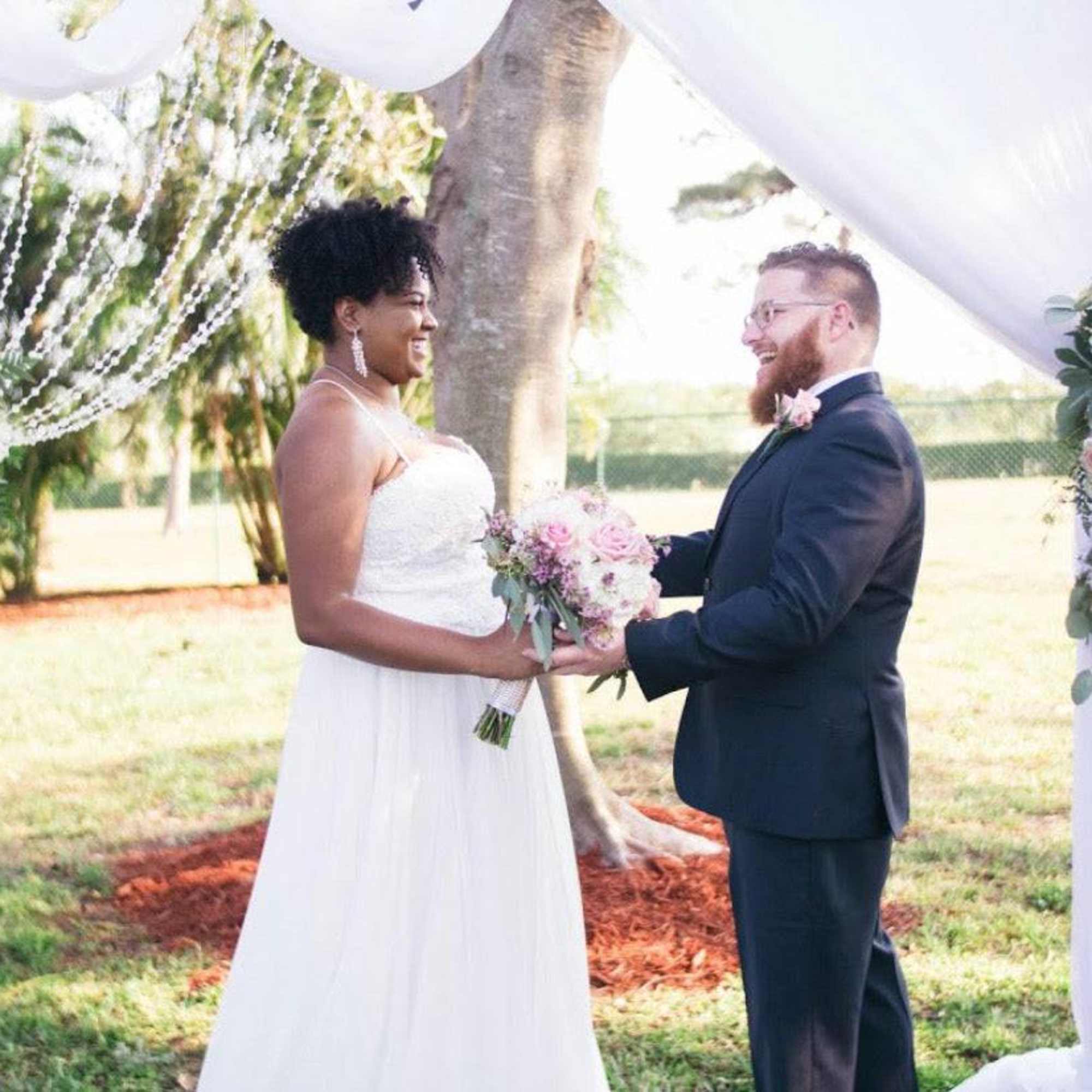 Bride and groom exchanging vows under a floral wedding arch