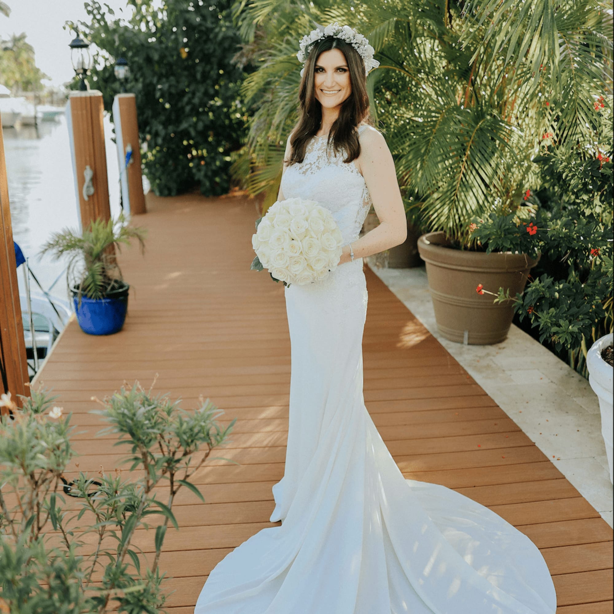 Bride holding a round bouquet of white roses and wearing a white floral crown