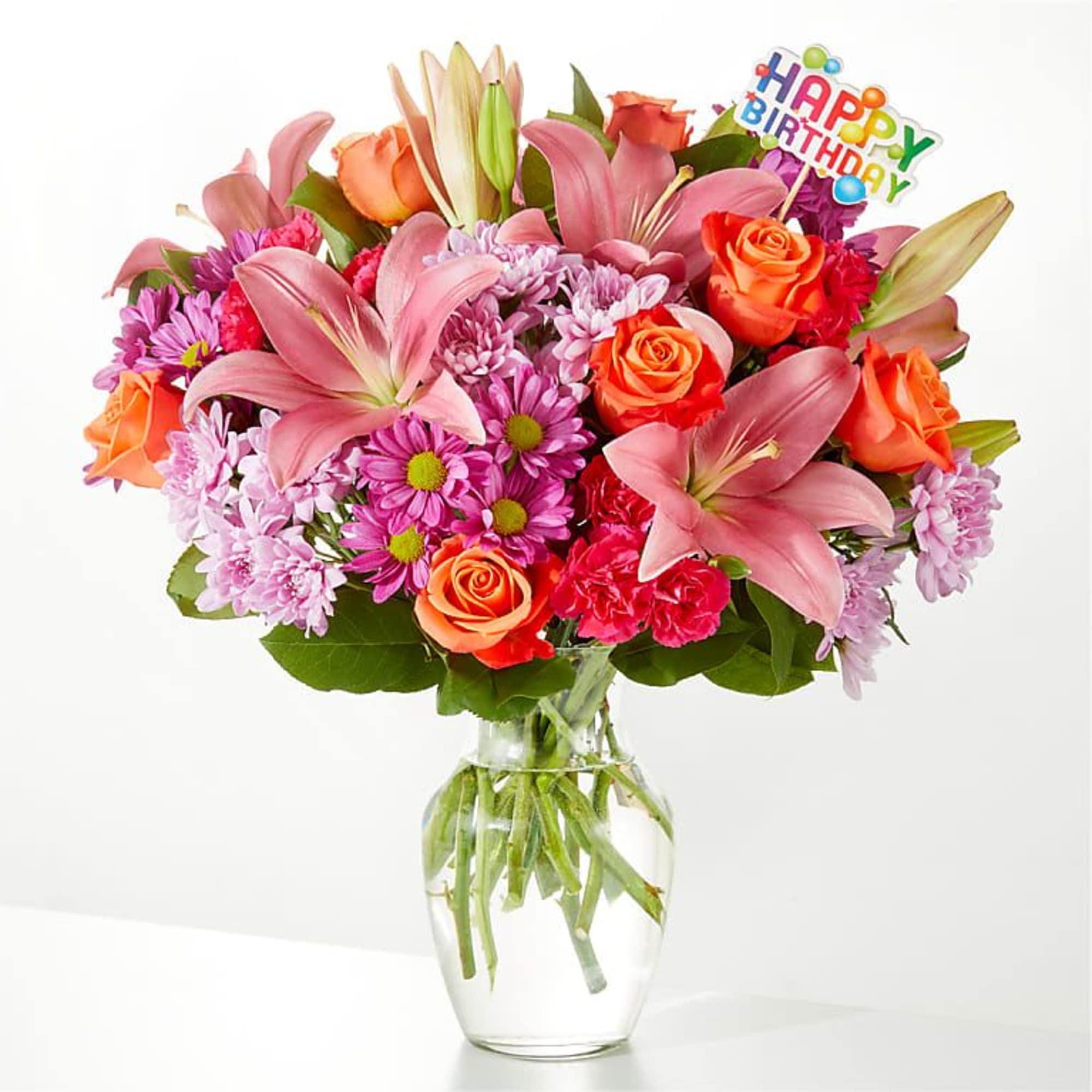 Mixed bouquet of pink lilies, orange roses, and purple daisies in a glass vase