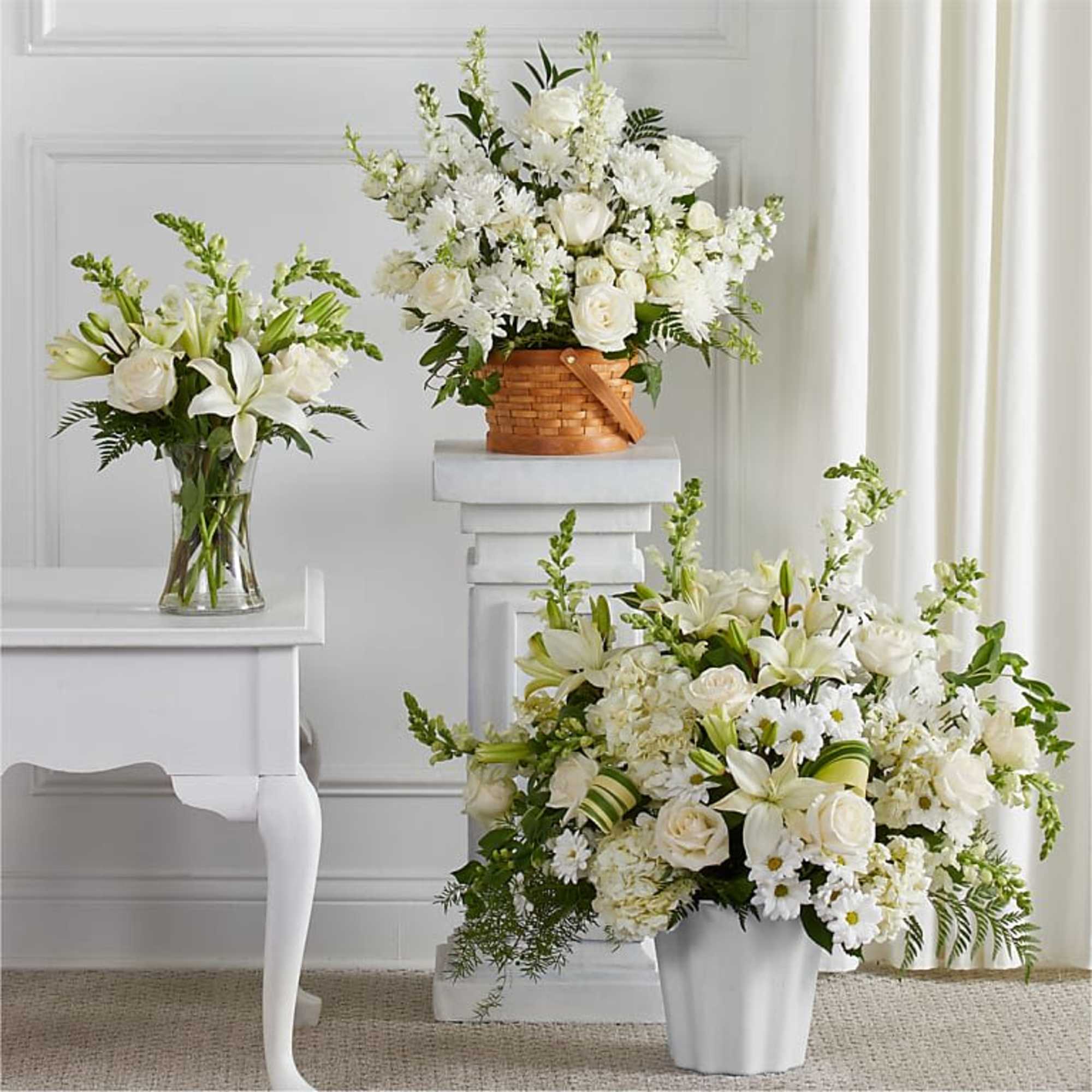 Three white floral arrangements in vases and a basket