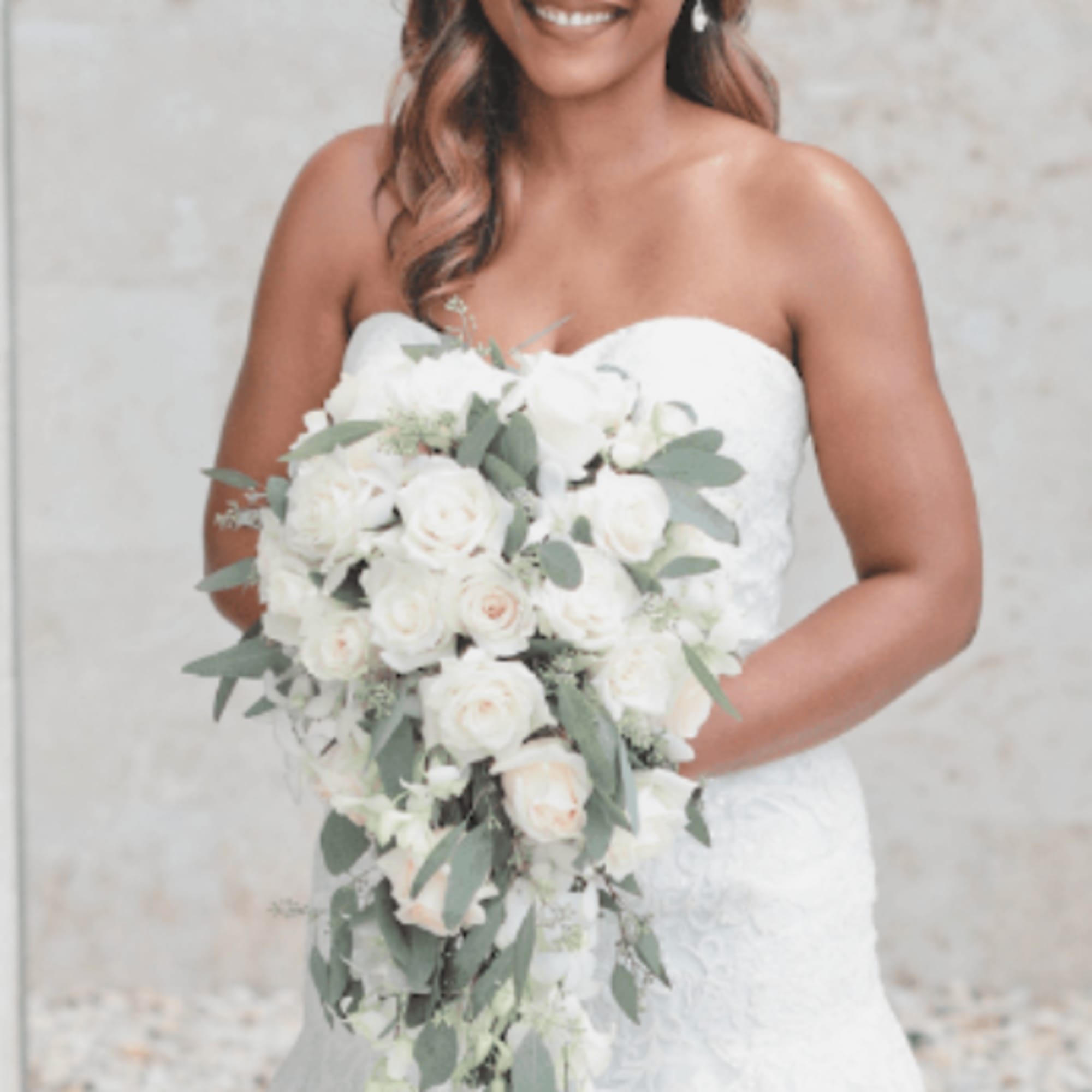Bride holding a cascading bouquet of white roses and greenery