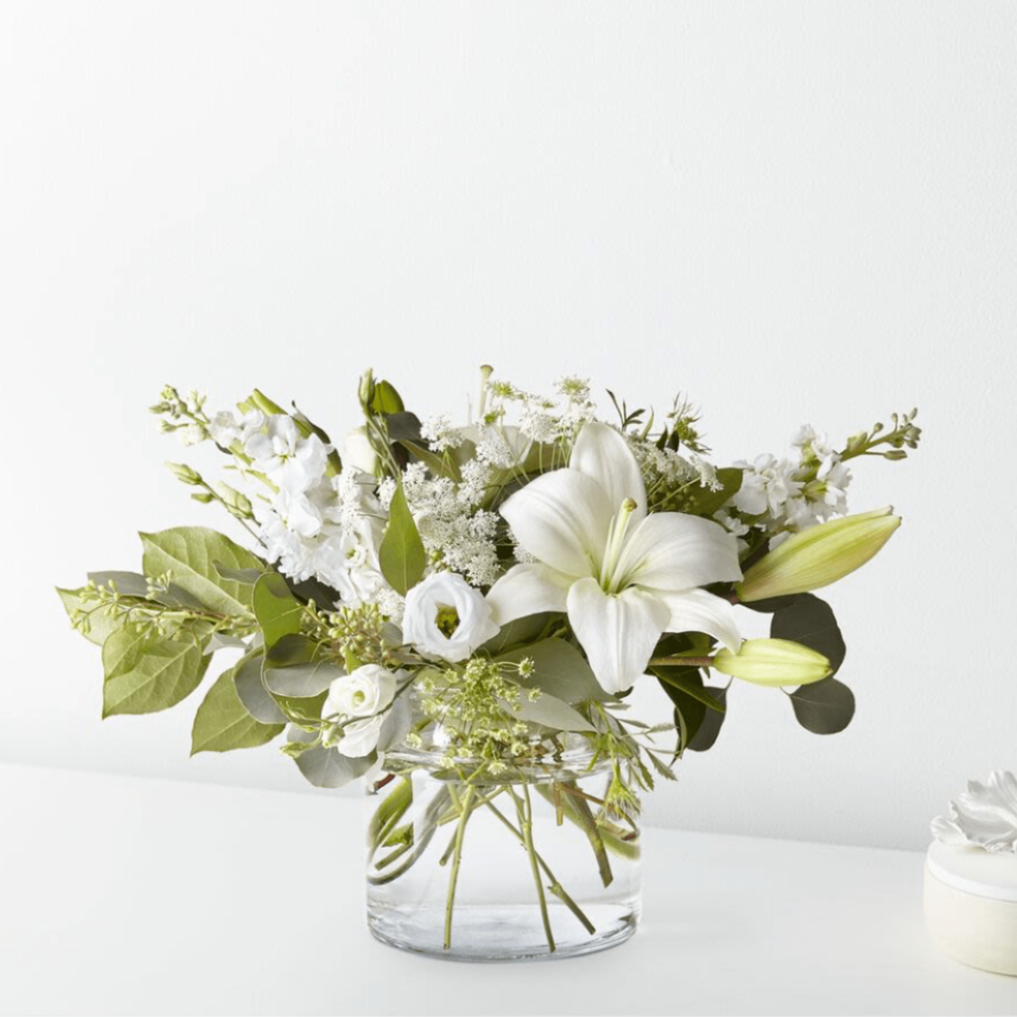 White lily and mixed white flowers in a clear glass vase