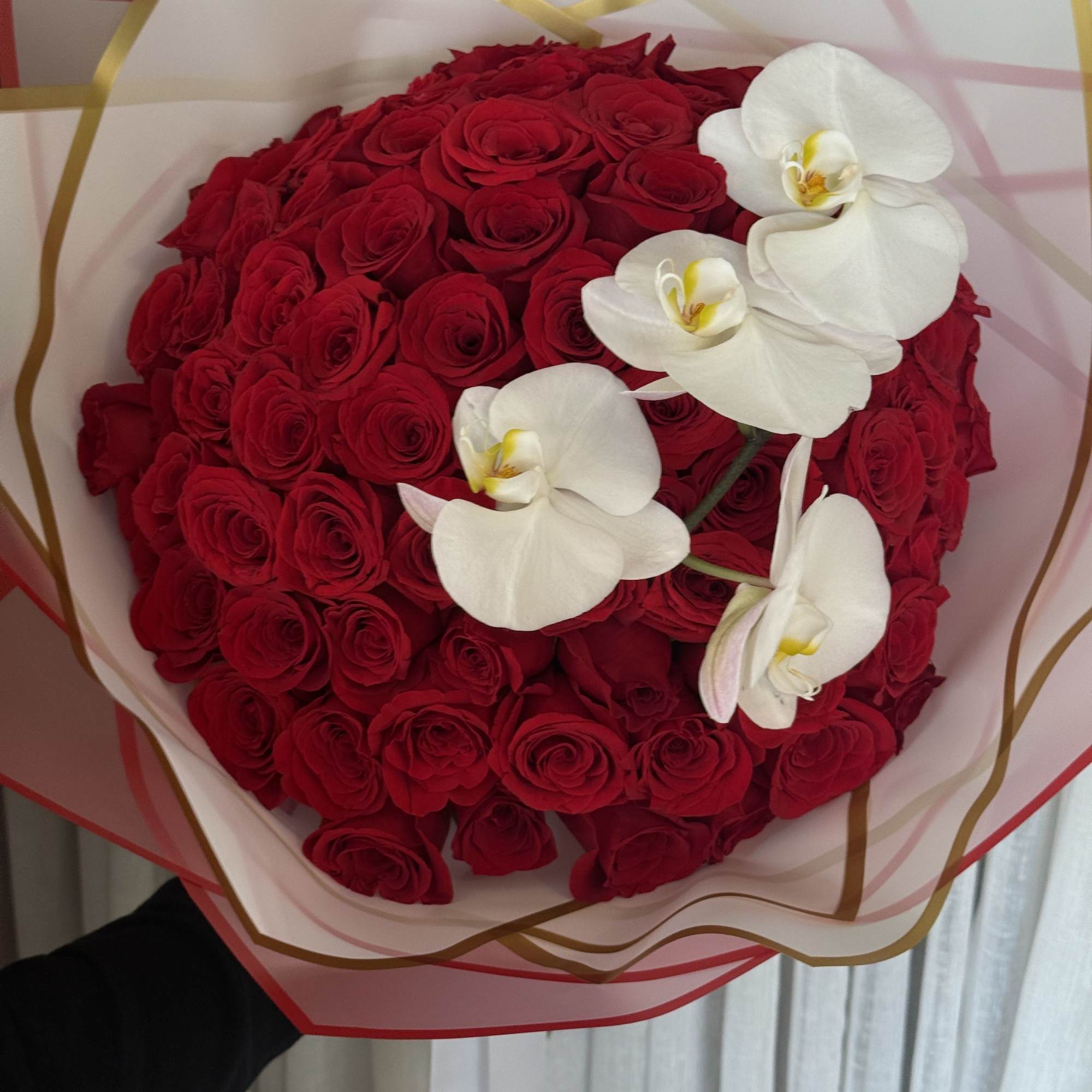 Bouquet of red roses with white orchids wrapped in translucent paper
