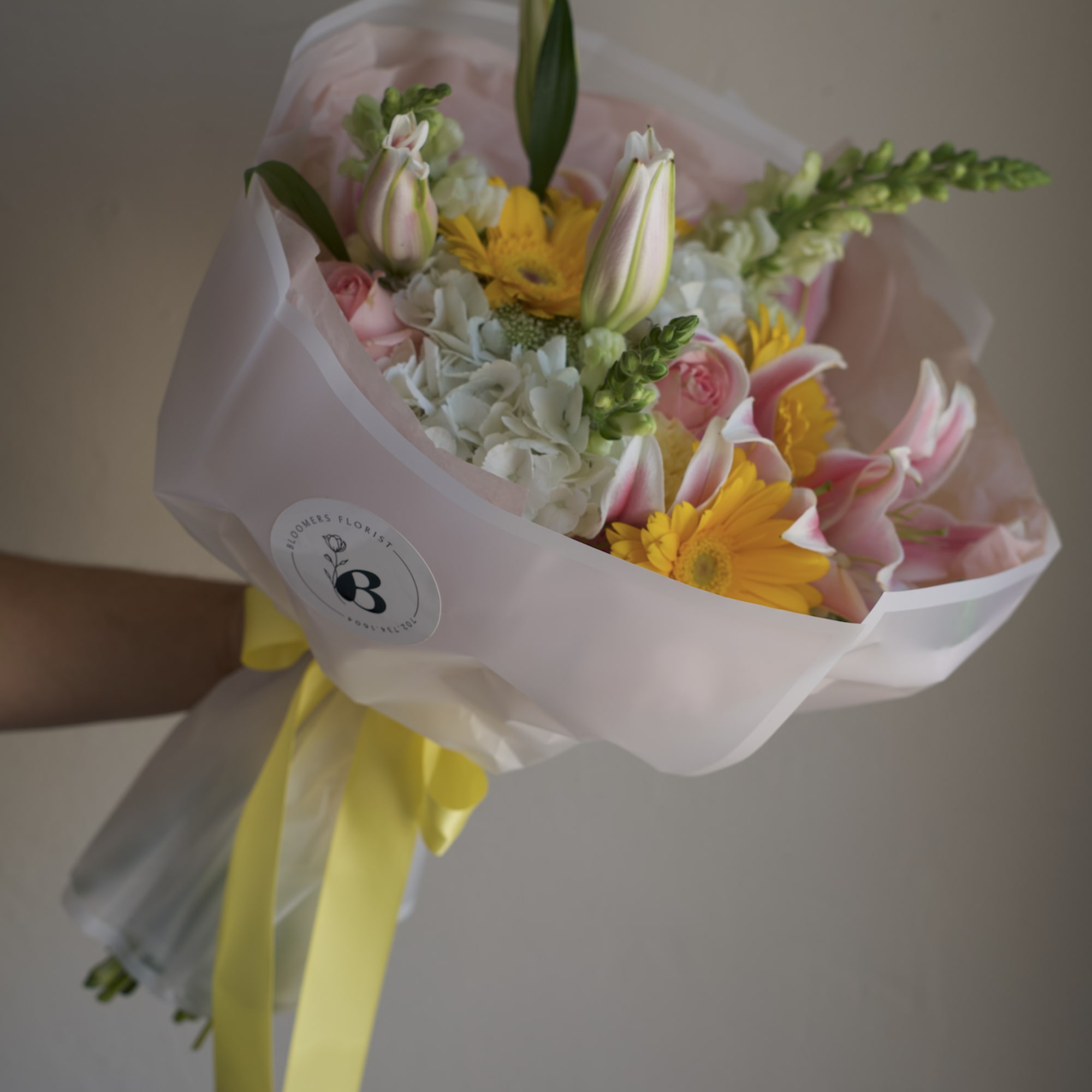 Bouquet of pink and yellow flowers wrapped in pale pink paper with a yellow ribbon