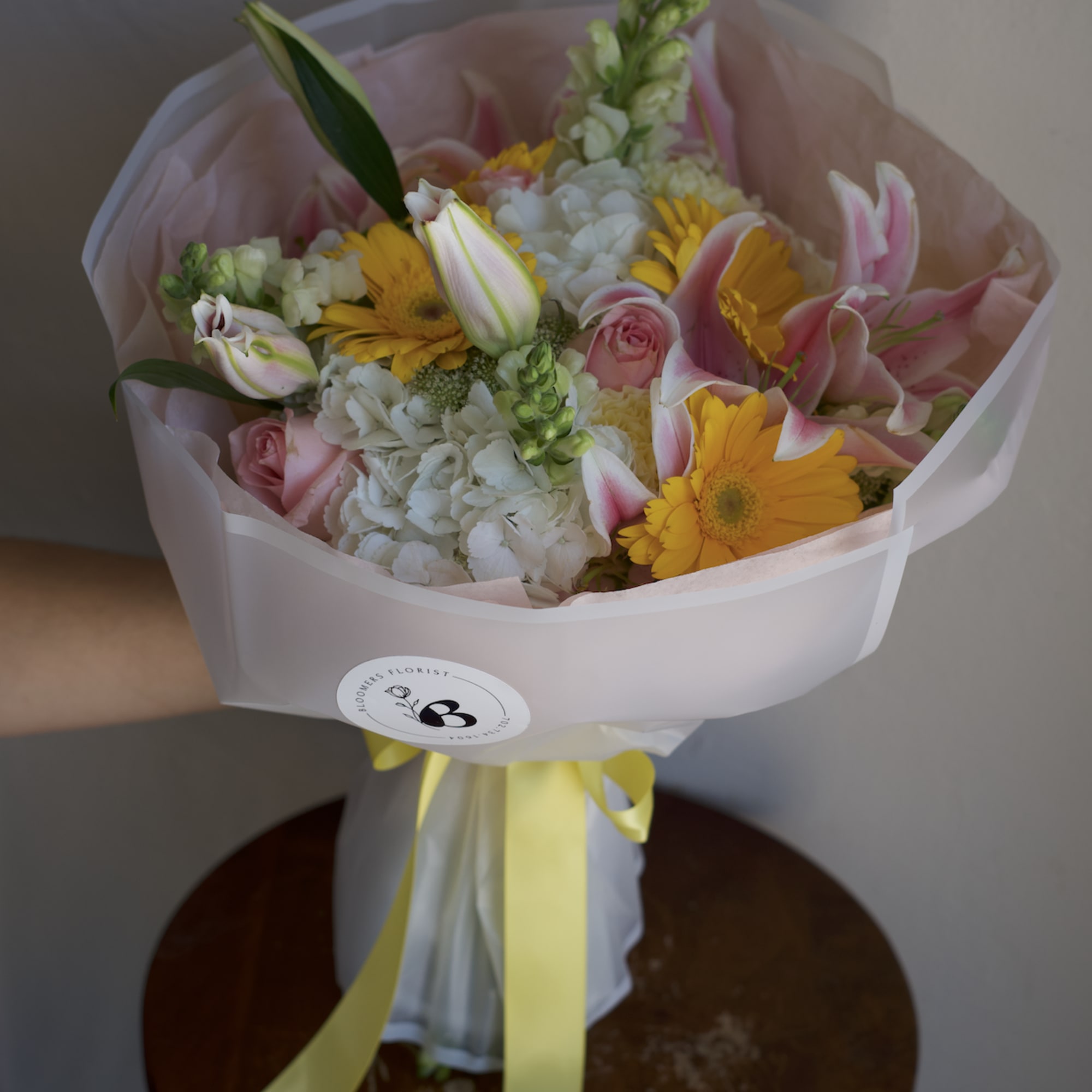 Bouquet of pink lilies, yellow daisies, and white blooms wrapped in pale pink paper