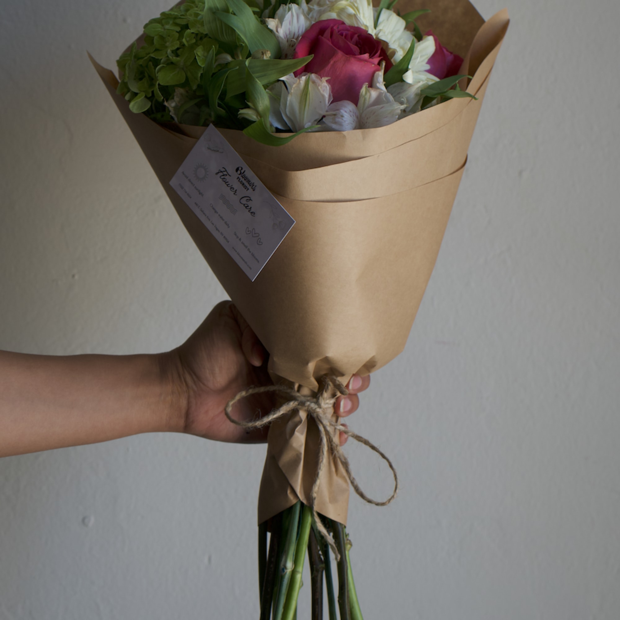 Handheld bouquet of pink roses and white flowers wrapped in brown paper