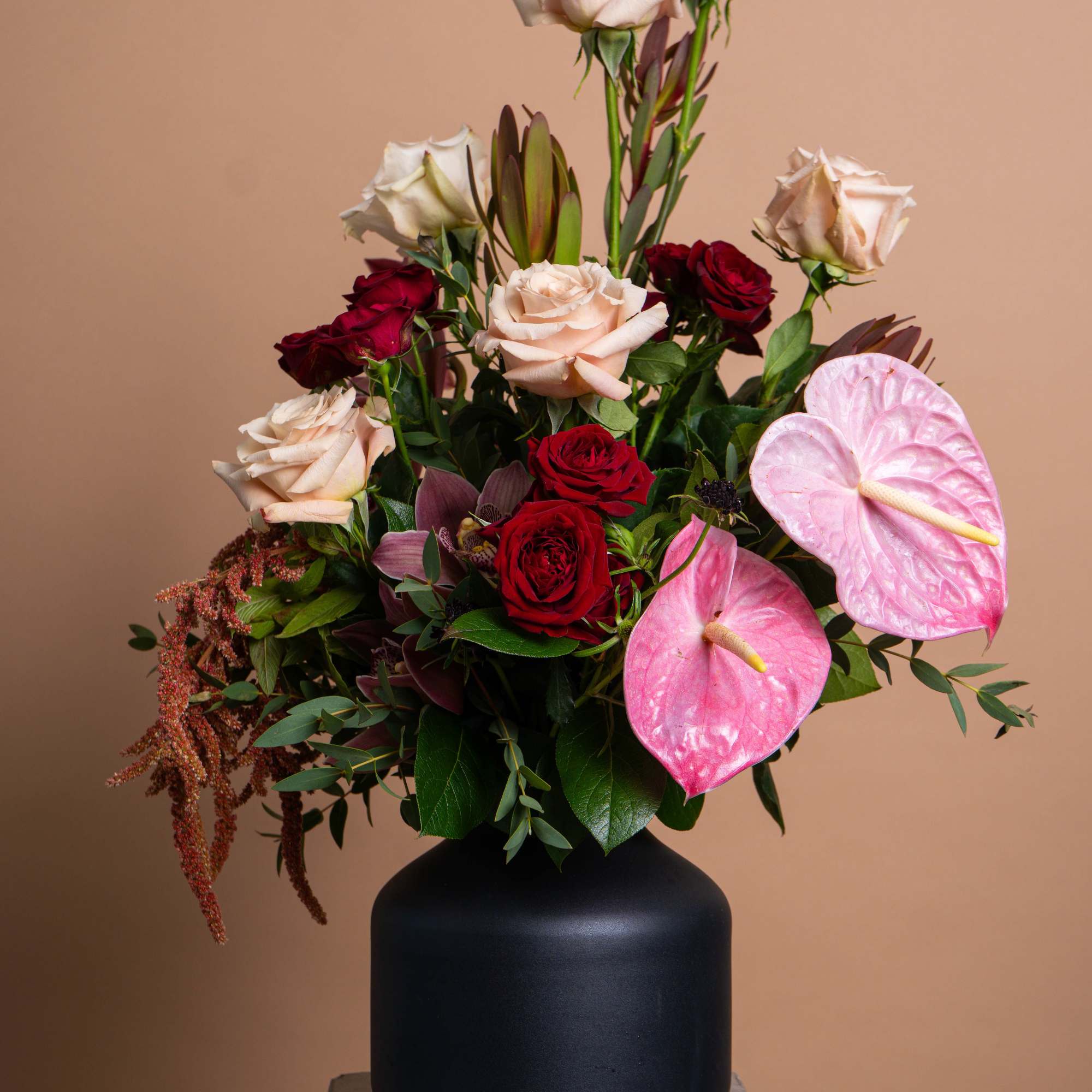 Mixed bouquet with roses and pink anthuriums in a black vase