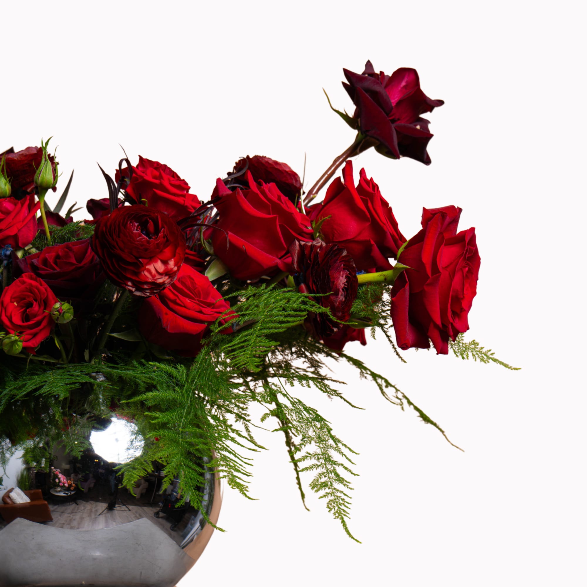 Red roses in a reflective silver vase with trailing greenery