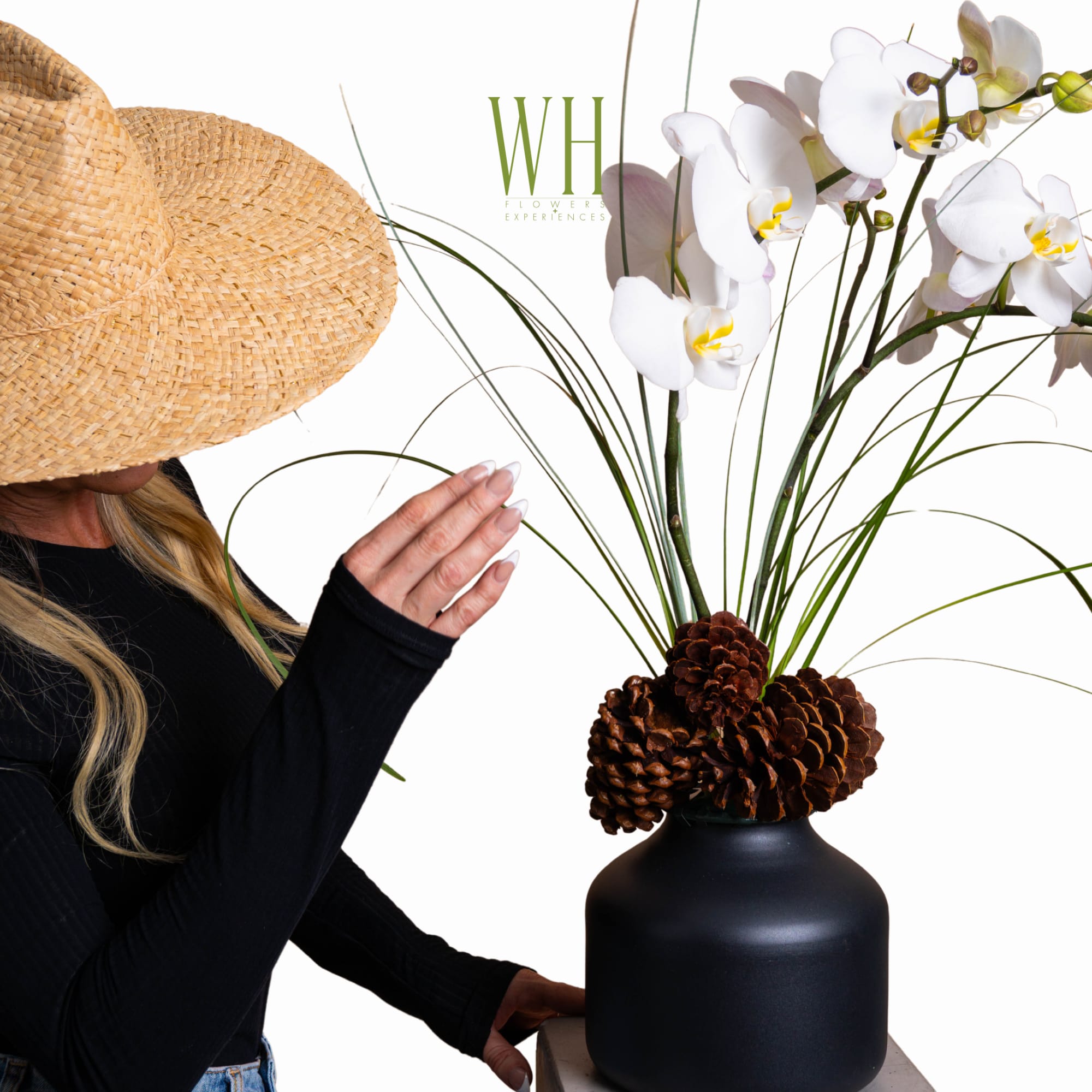 White orchids in a black vase with pinecones and tall grass