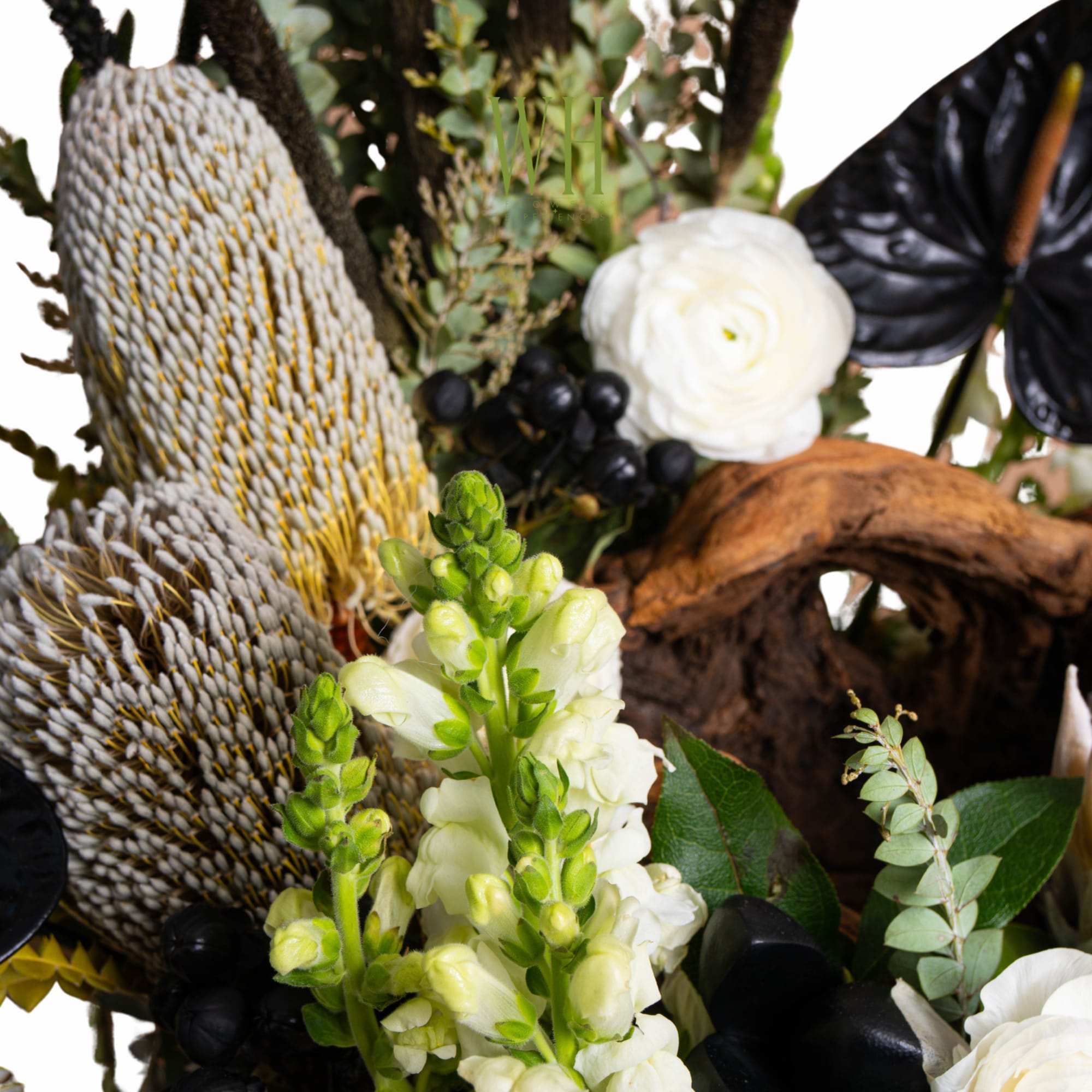 Close-up of a floral arrangement with white blooms, black anthurium, and textured seed pods