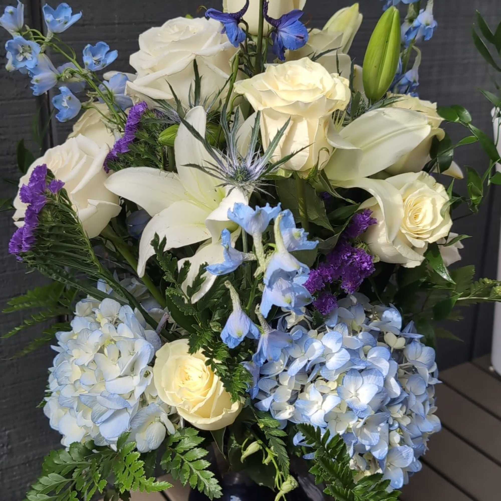 A blue and white arrangement featuring roses, tulips, and delphinium. Send this