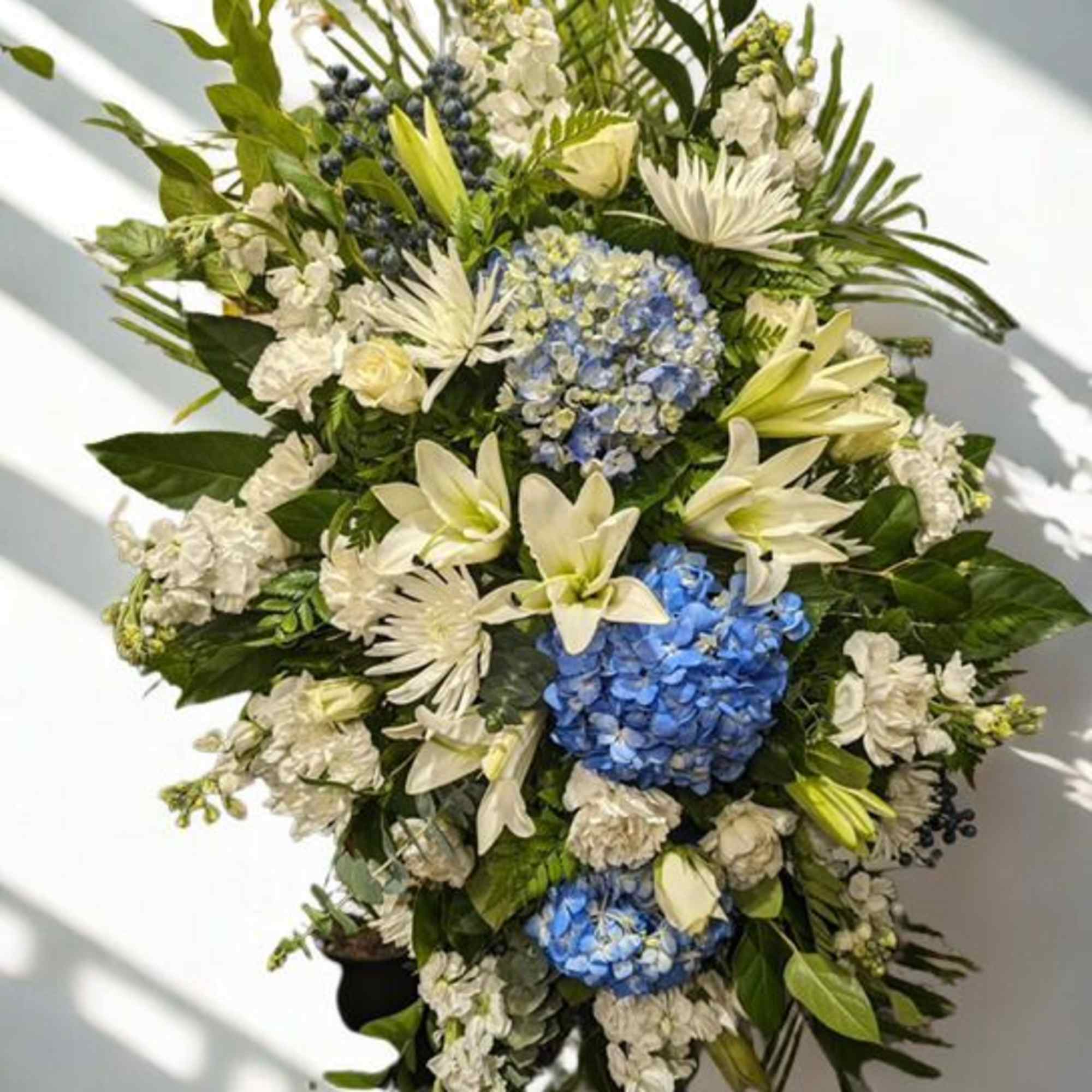 Large floral standing spray with blue hydrangeas, white lilies, and white blooms