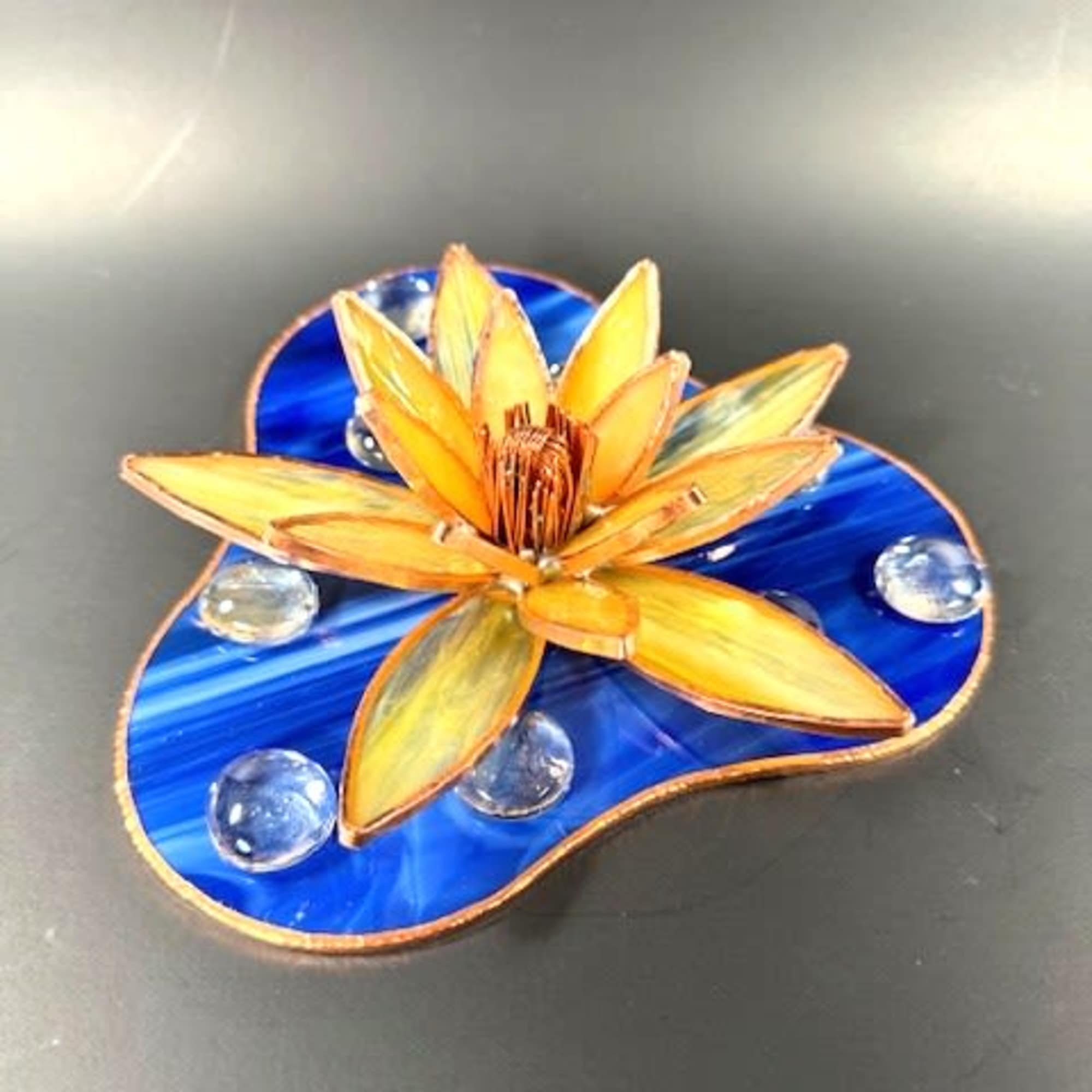 A sunlit, sculptural flower in warm yellow and orange stained glass catches