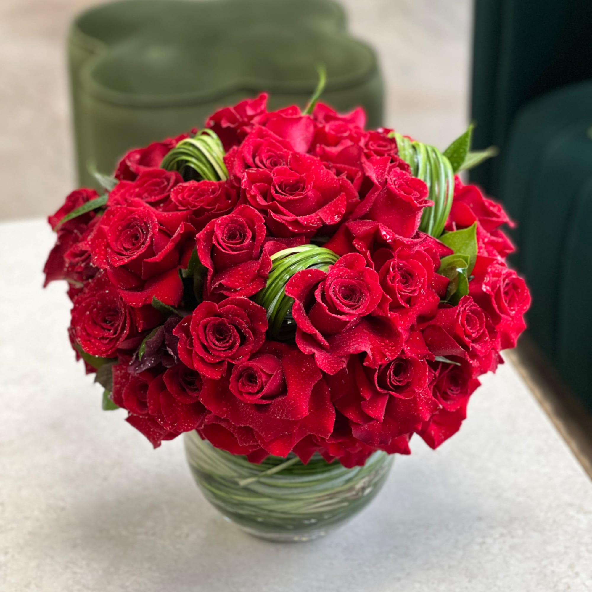 Red rose bouquet in a clear glass vase with green decorative loops