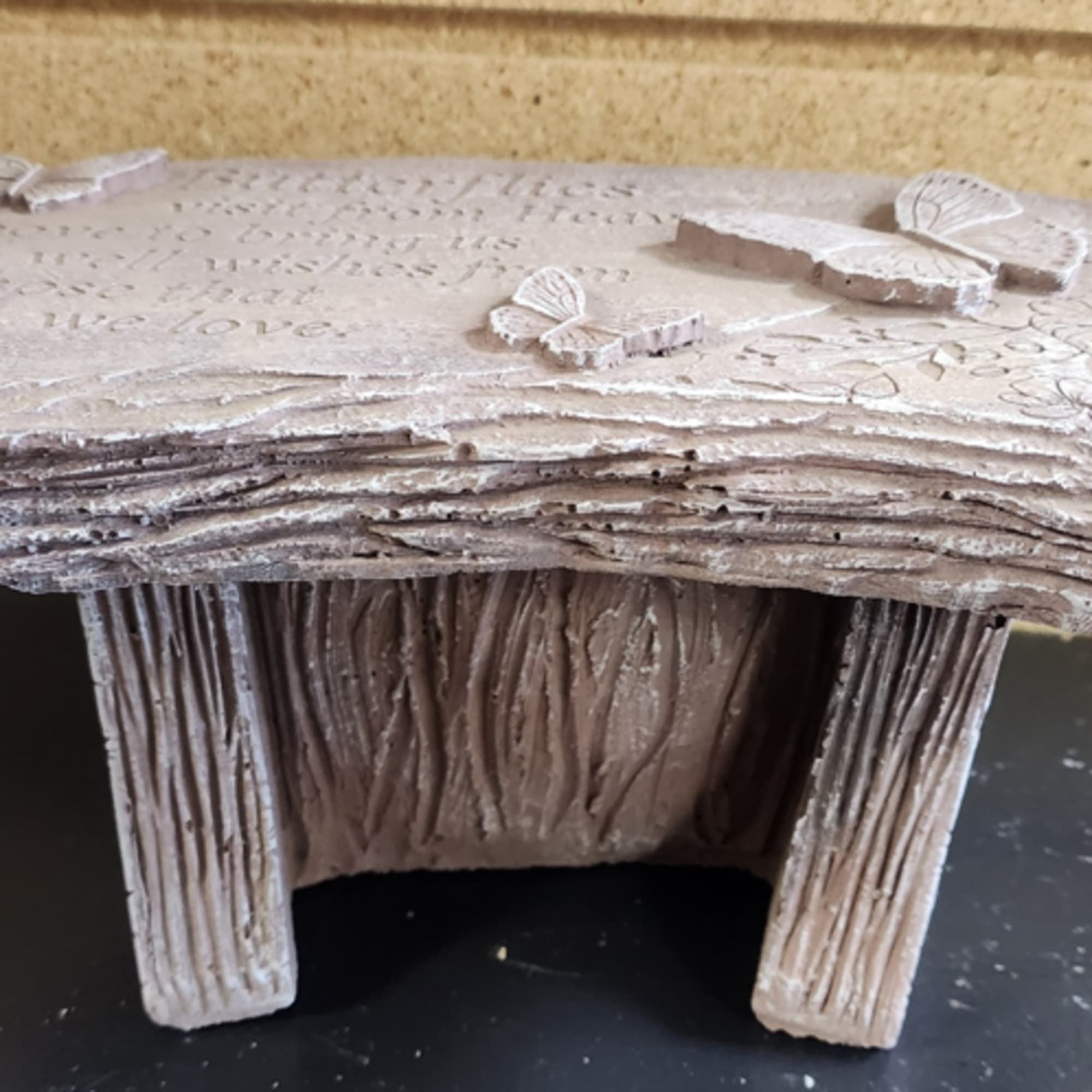 Small faux-stone memorial bench with carved butterflies and engraved inscription