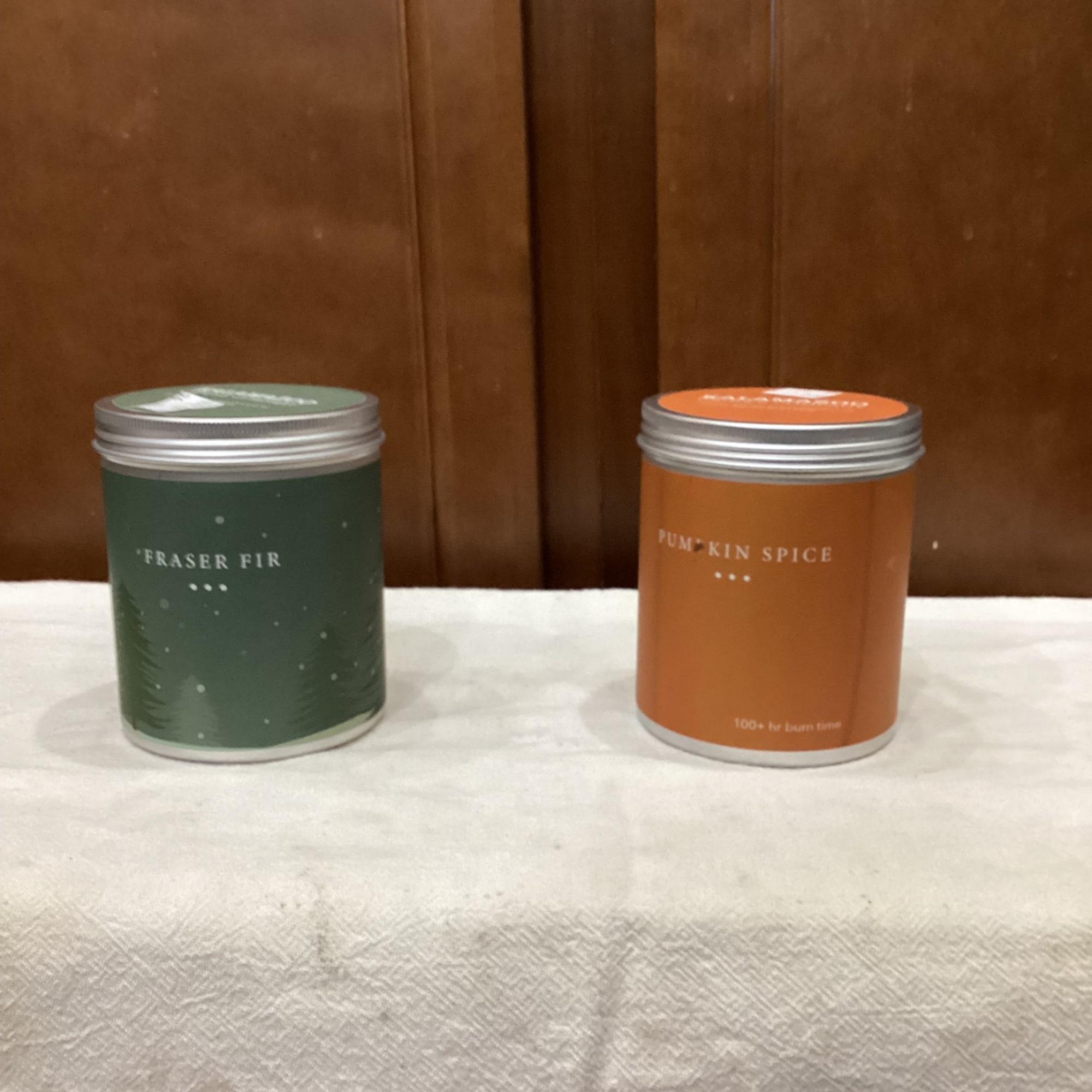 Two scented candles in metal tins, one green and one orange.