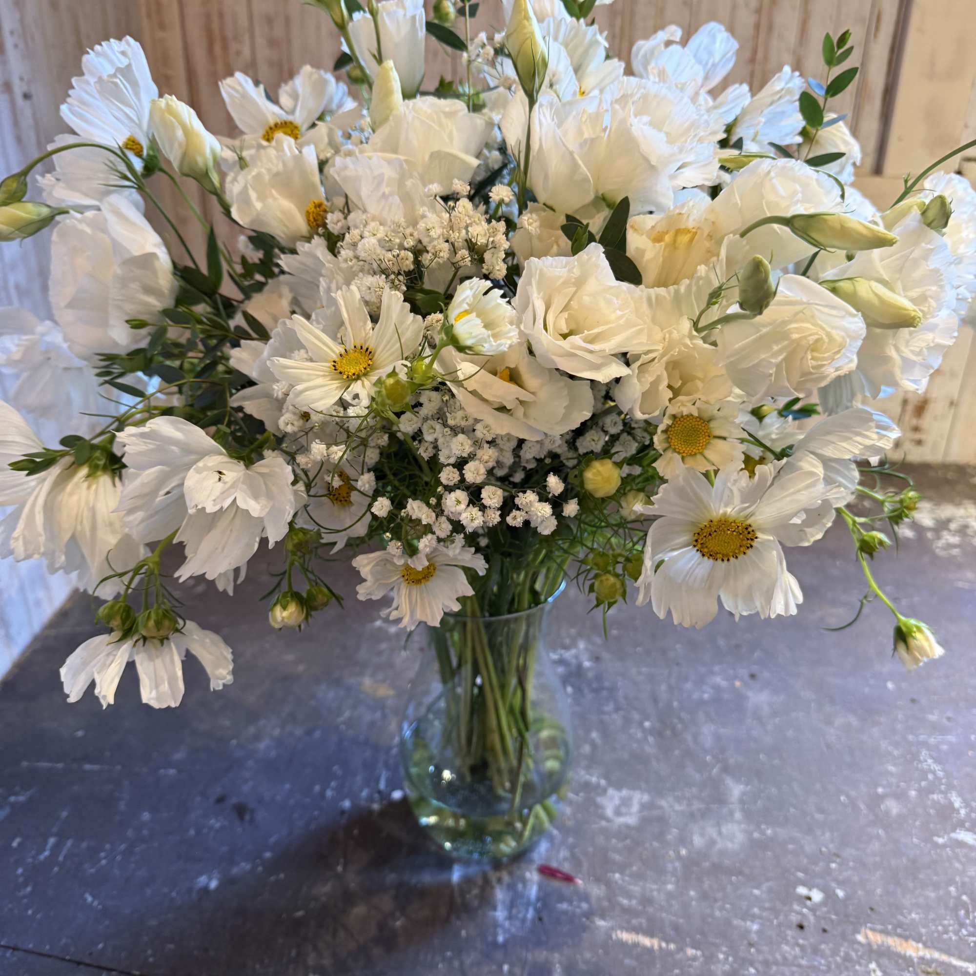 Tall glass vase of white daisylike blooms and lisianthus with yellow centers in a loose, airy arrangement
