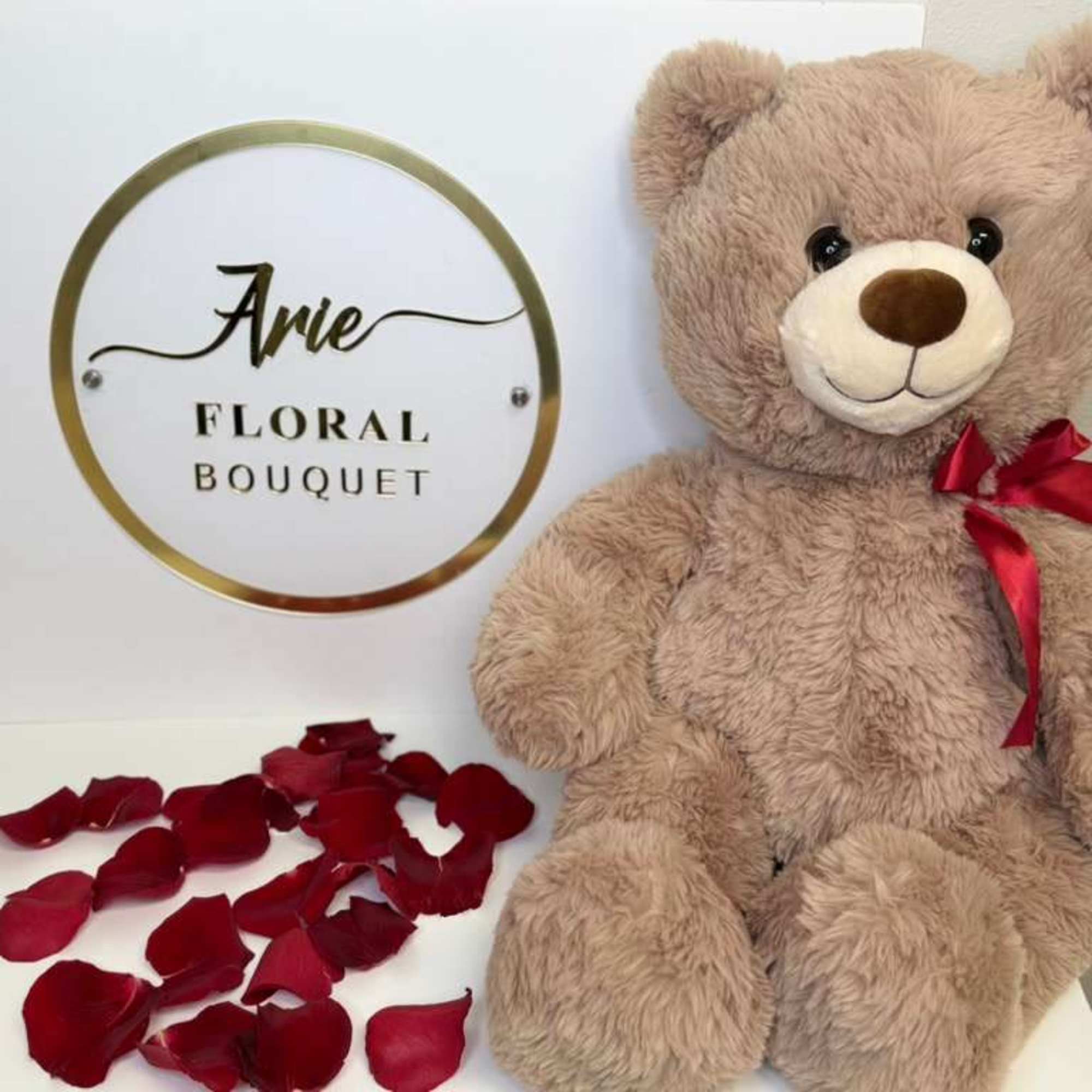 Teddy bear with a red ribbon beside scattered rose petals