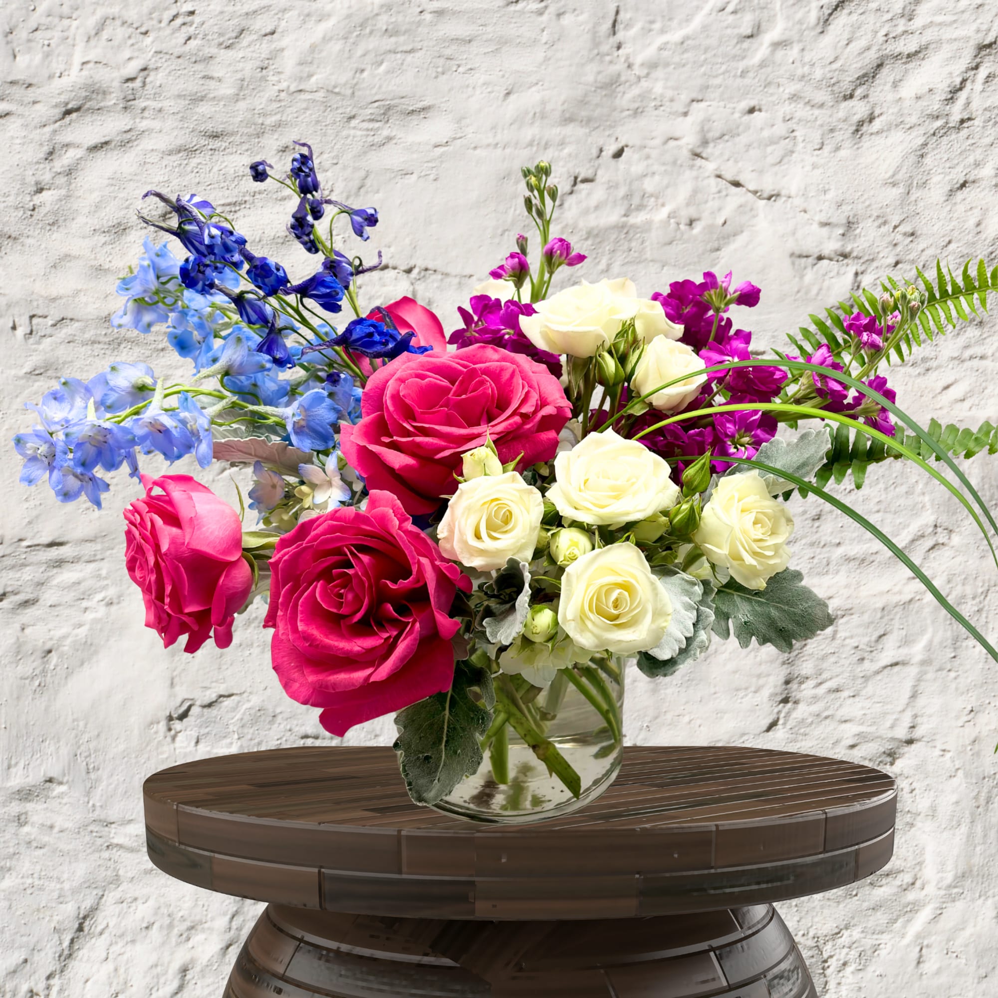Mixed bouquet of pink, white, blue, and purple flowers in a glass vase