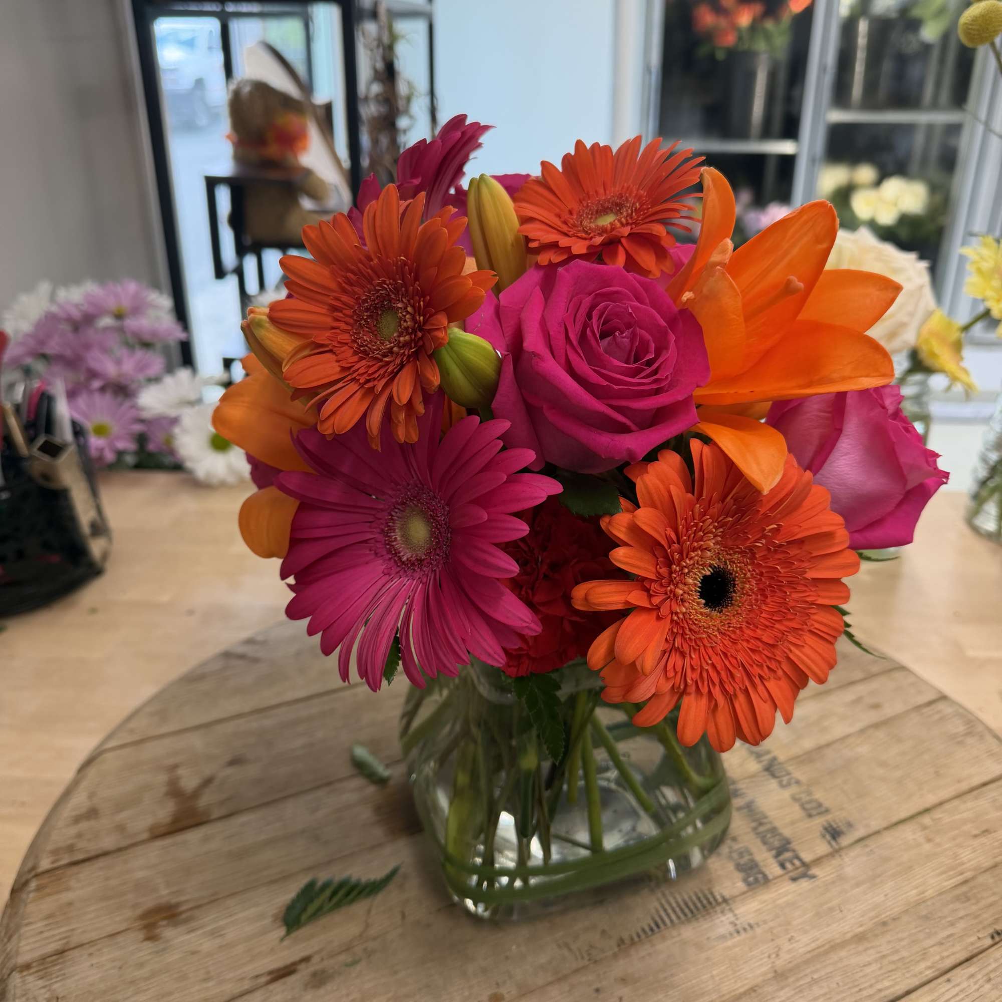 Bright mixed bouquet of pink roses, orange gerberas, and lilies in a glass vase
