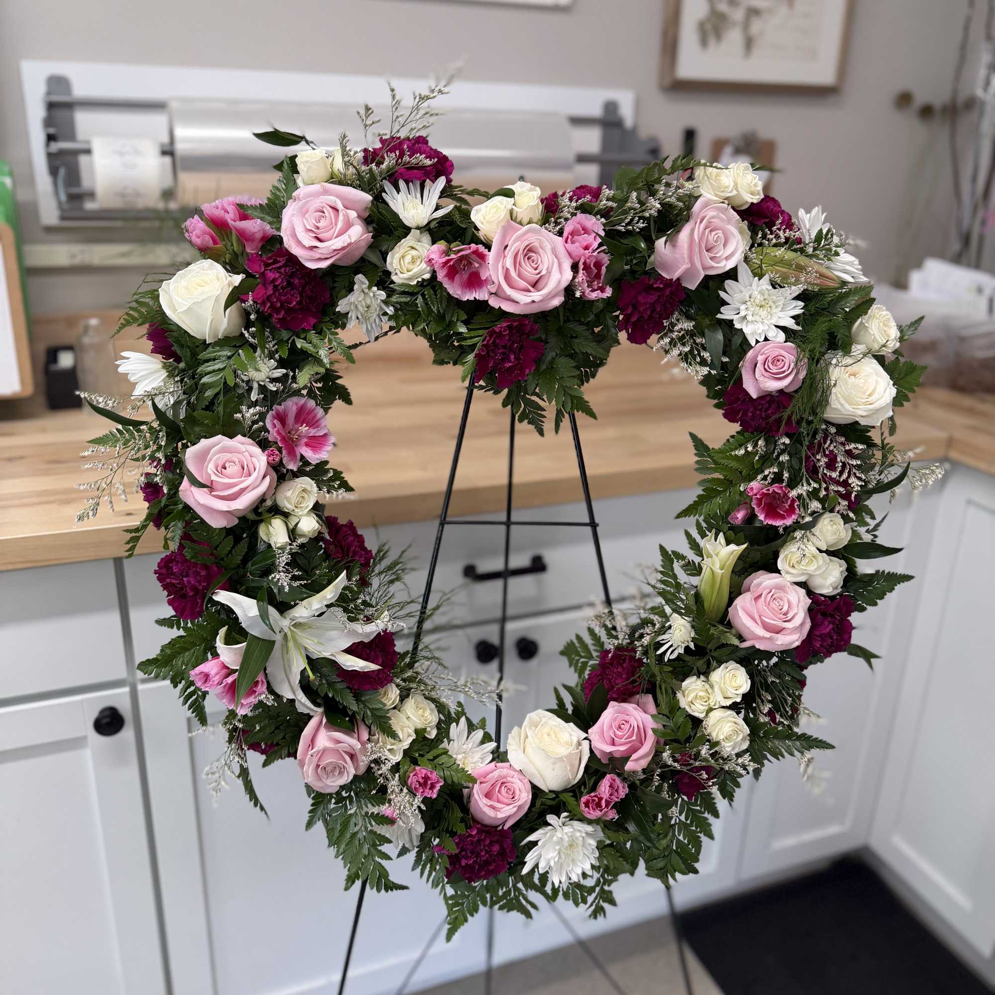 Heart-shaped floral wreath with pink and white roses on a stand
