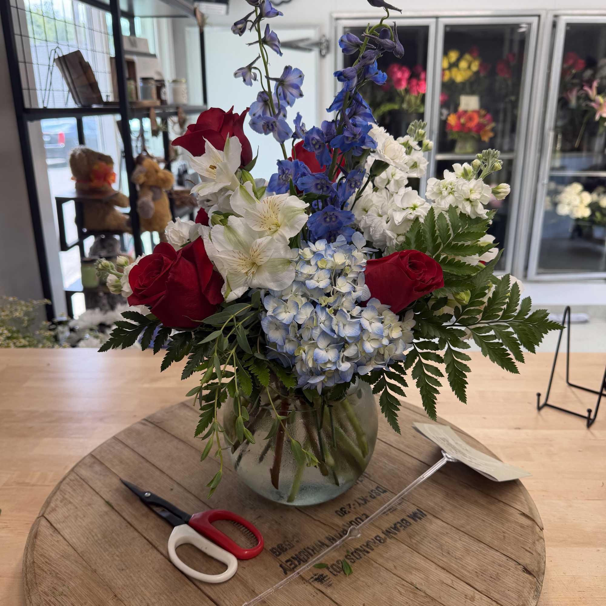 Mixed bouquet with red roses, blue delphinium, white alstroemeria, and hydrangea in a glass vase