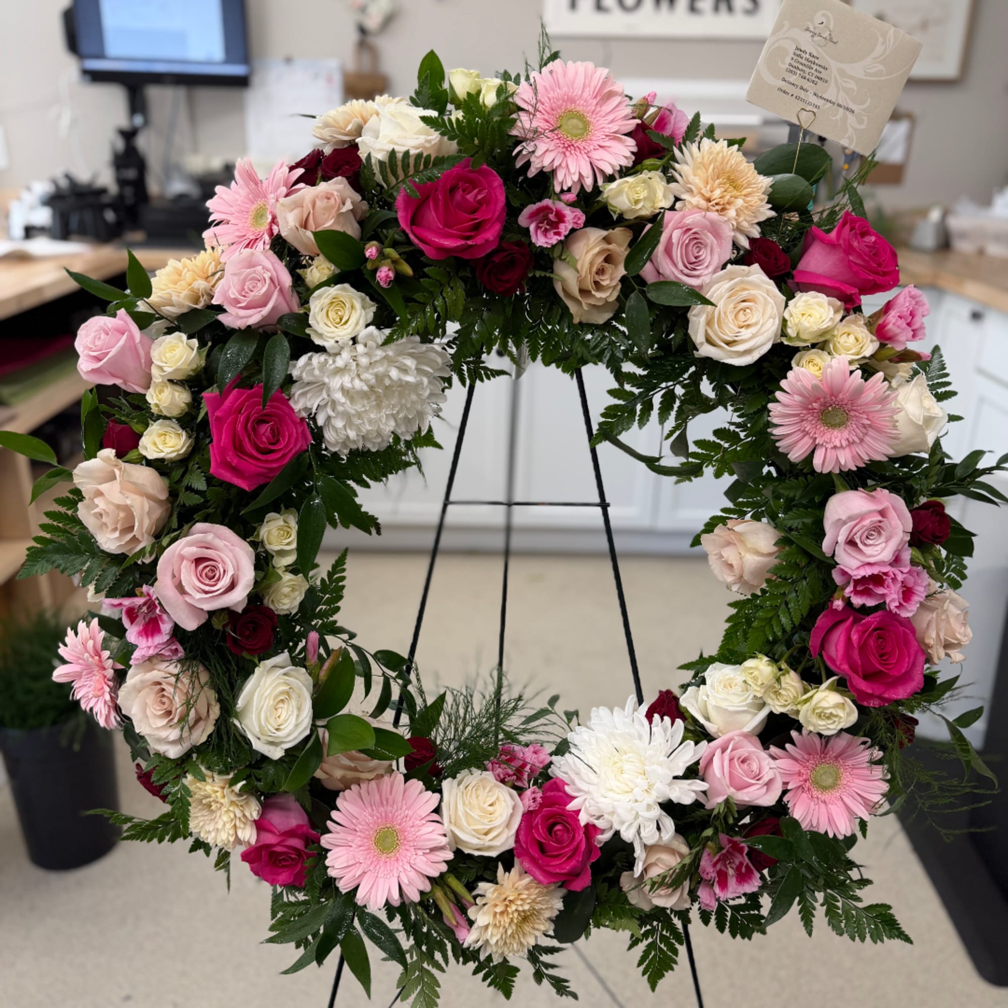 Heart-shaped floral wreath with pink and white roses and daisies on a stand