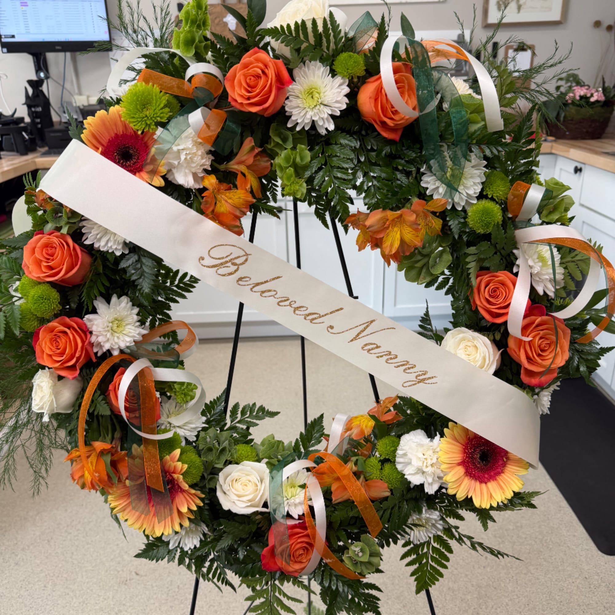 Floral wreath with orange roses, gerbera daisies, and white blooms on an easel