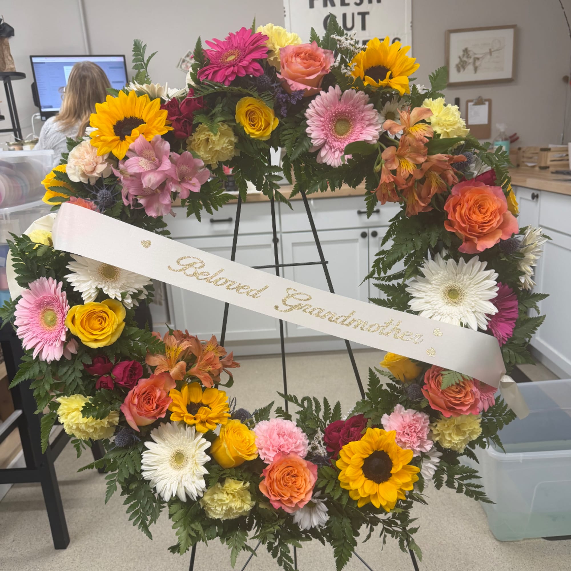 Colorful floral wreath on an easel with a ribbon reading Beloved Grandmother.