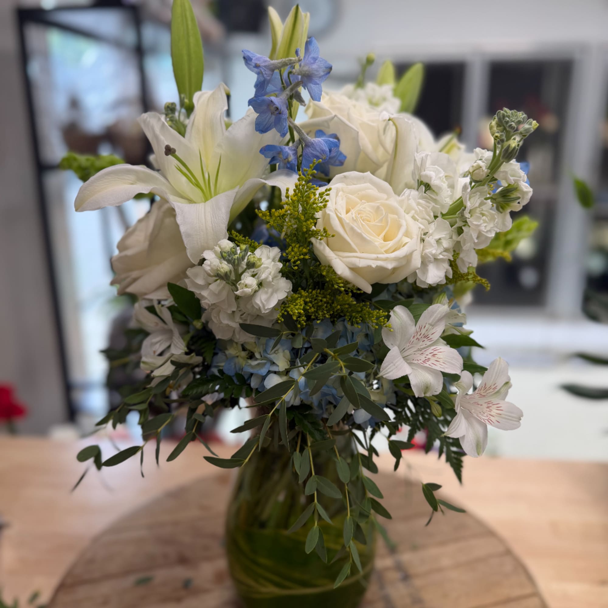 White lilies and roses in a green glass vase with blue flowers