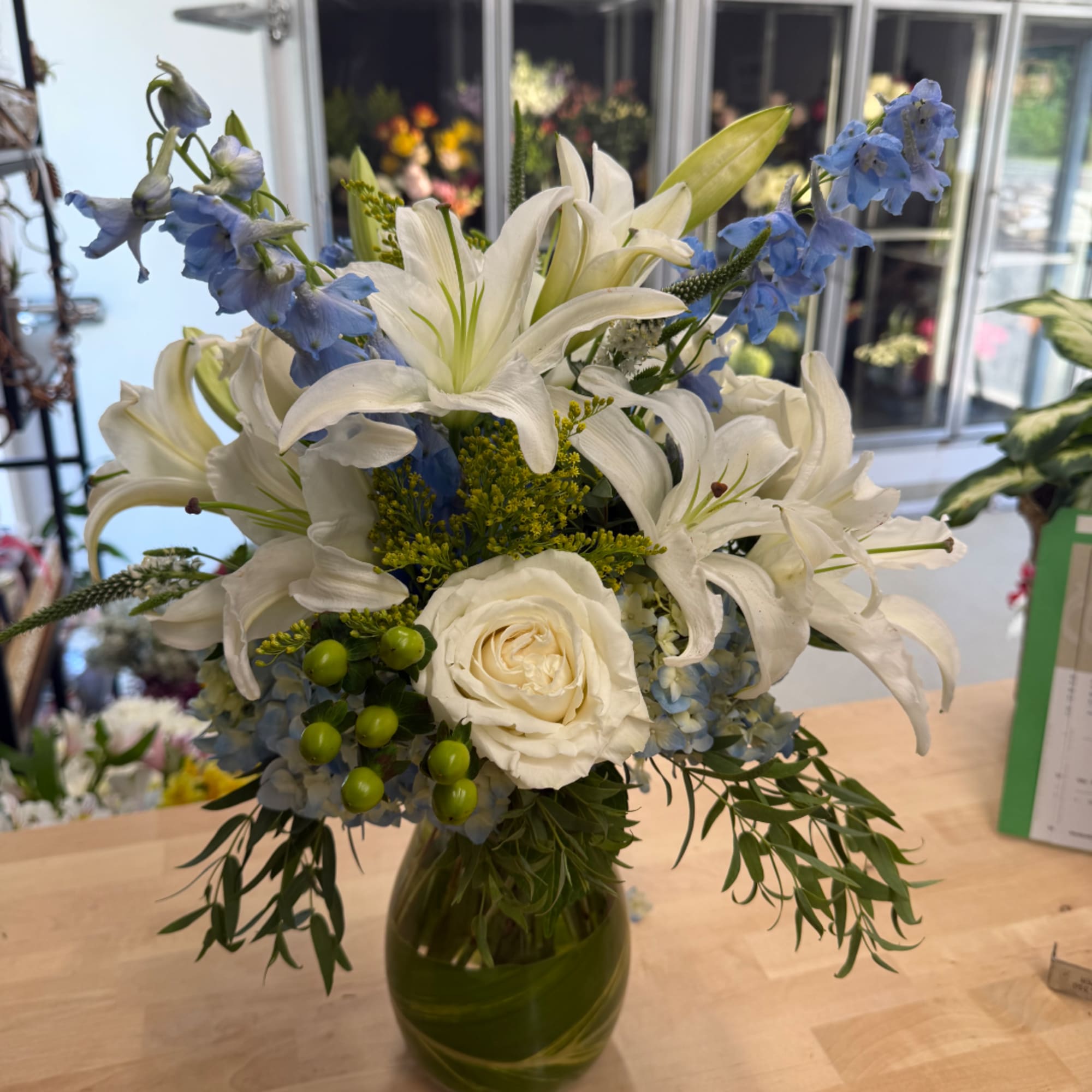 White lilies and roses with blue flowers in a green glass vase
