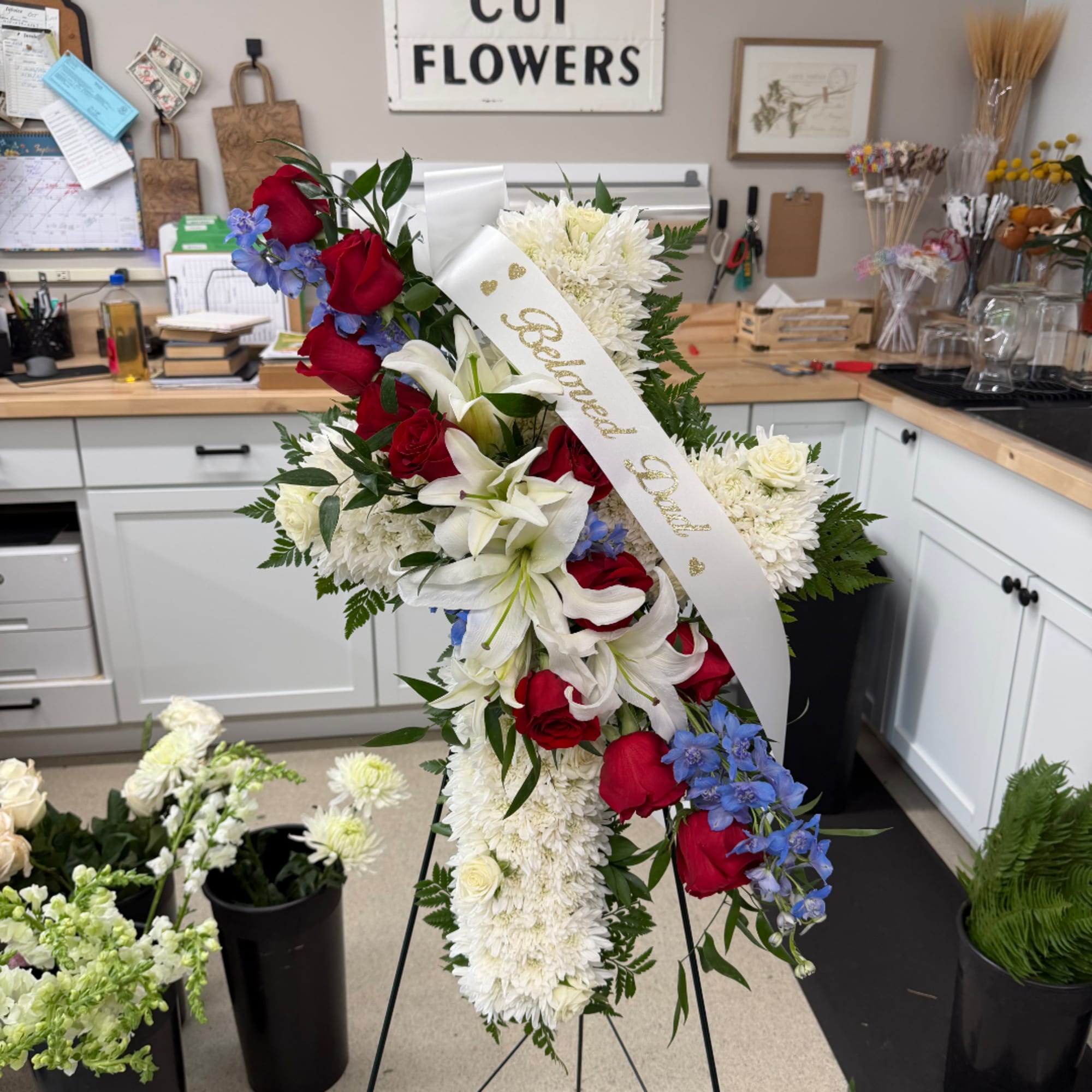 Standing floral spray with red roses, white lilies, and blue flowers on an easel