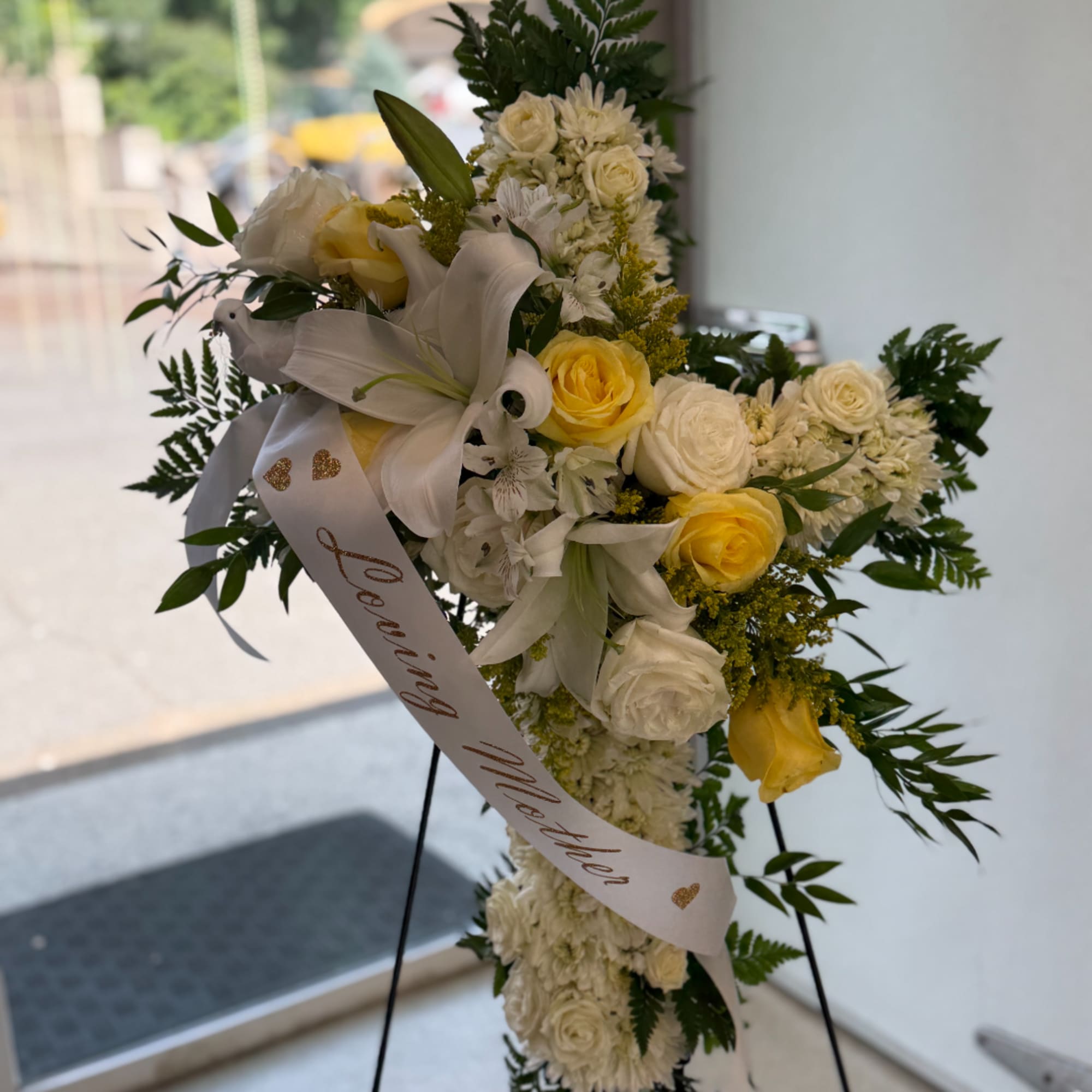 White and yellow floral standing spray with a ribbon on an easel