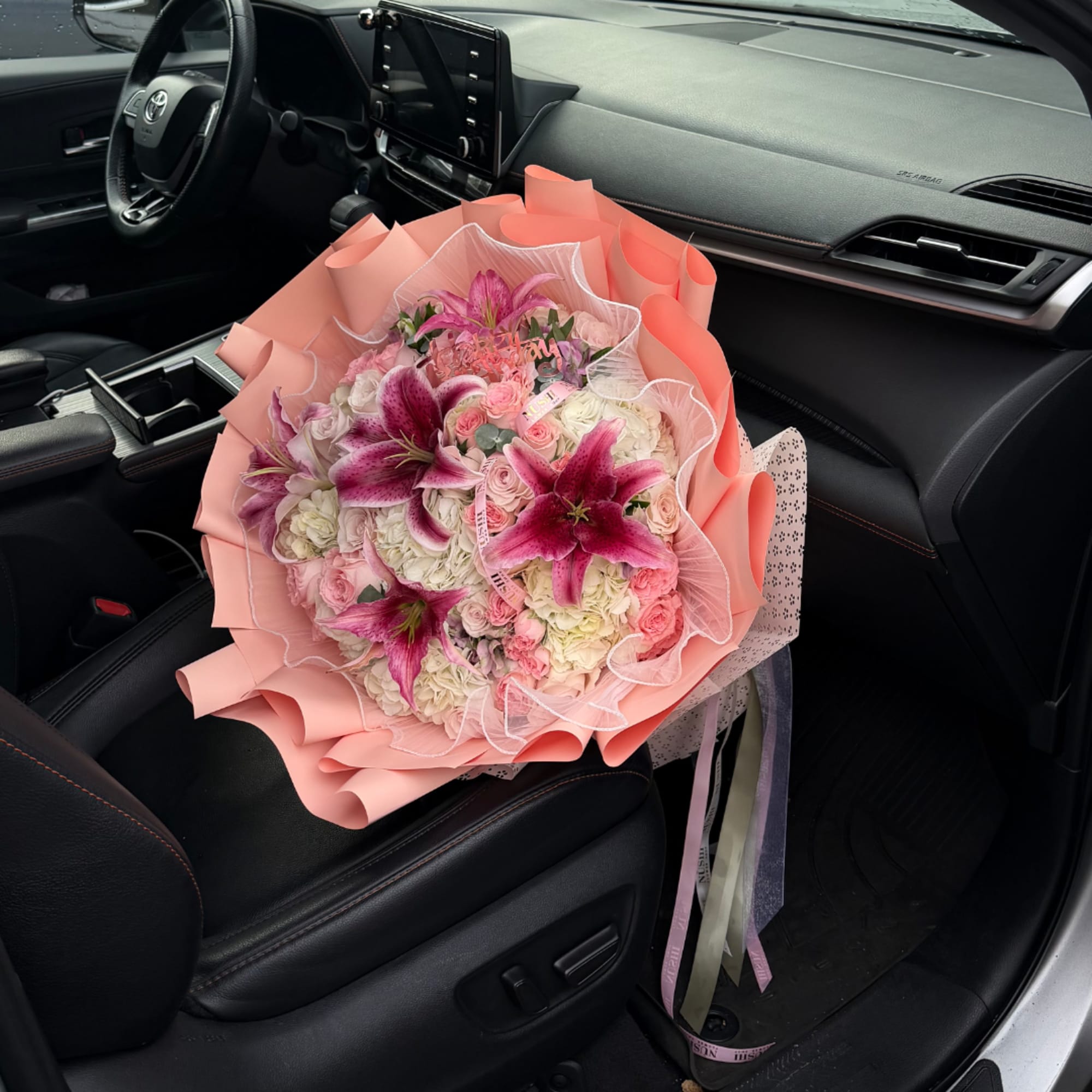 Pink and white bouquet with lilies and roses wrapped in peach paper on a car seat
